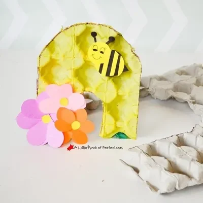 A paper bumble bee and flowers in front of an egg carton hive