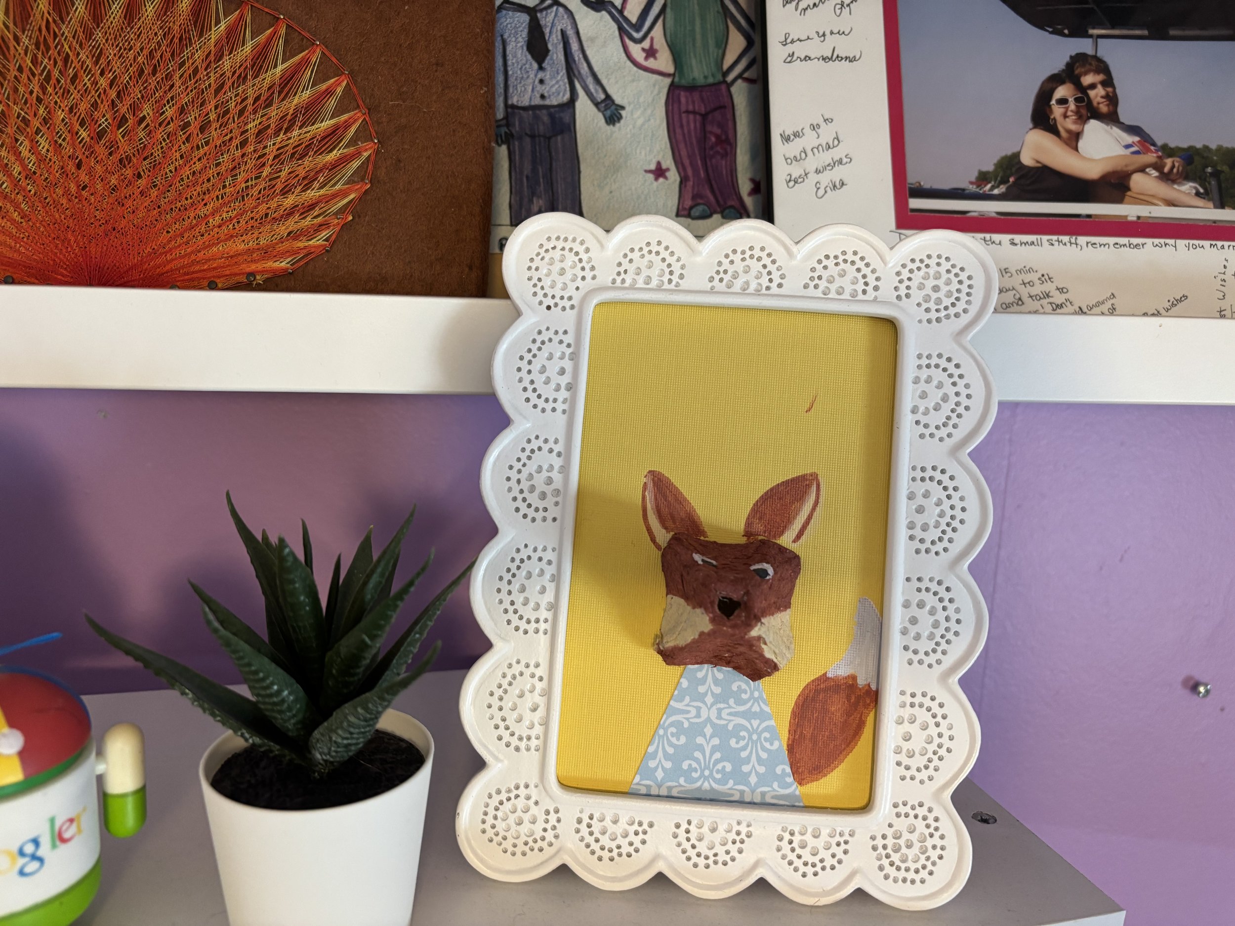 A portrait of a fox made from an egg carton in a decorative white frame on a shelf.