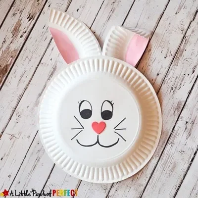 A smiling paper plate rabbit on a wooden table.