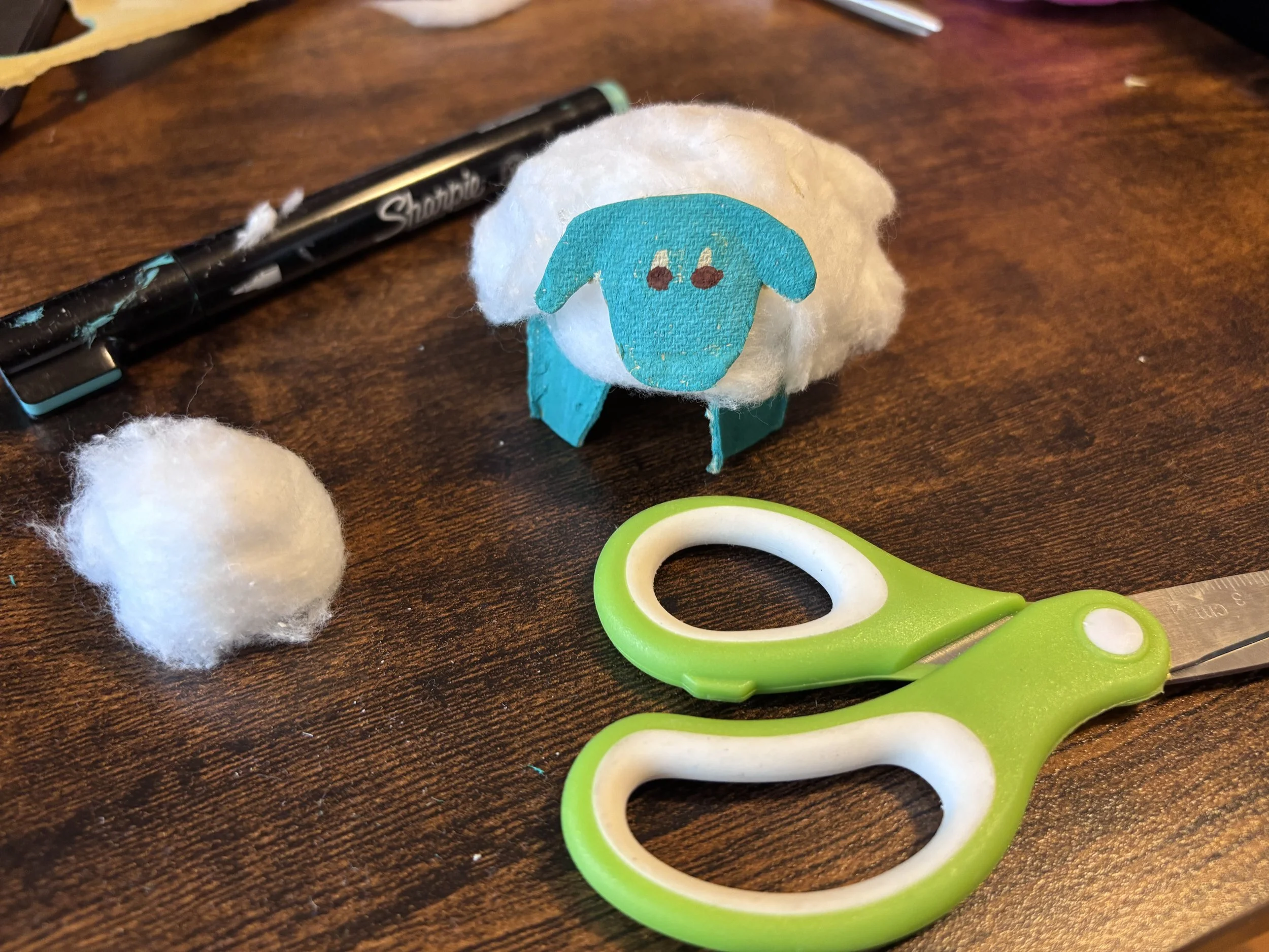 A sheep made from an egg carton and cotton balls with a marker, scissors, and cotton ball.