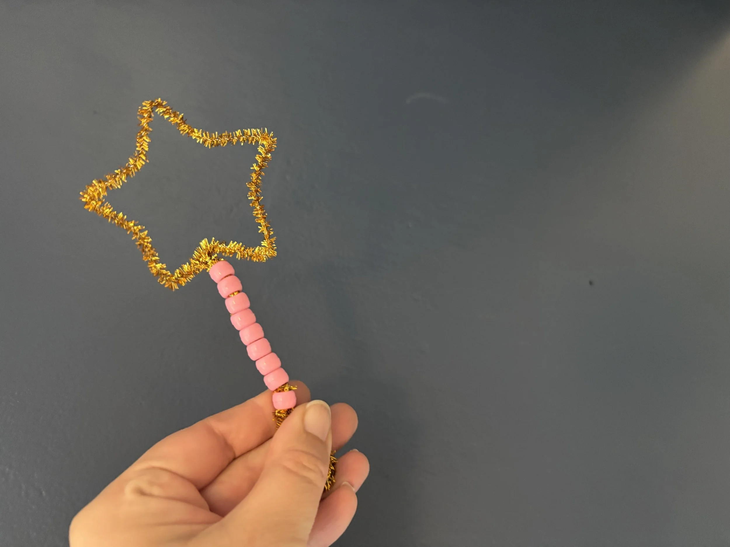 A star-shaped bubble wand made from a sparkly gold pipe cleaner decorated with pink pony beads.