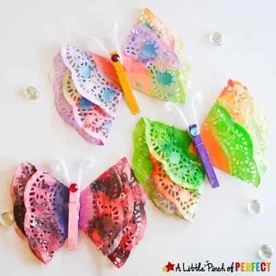 Three butterflies made from painted doilies and clothespins on a white background.