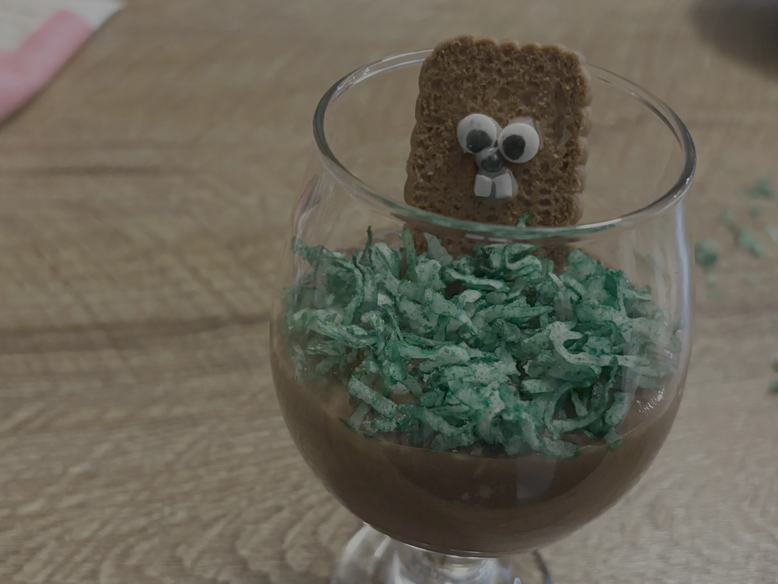 A cookie groundhog in chocolate pudding dirt and green coconut flake grass.