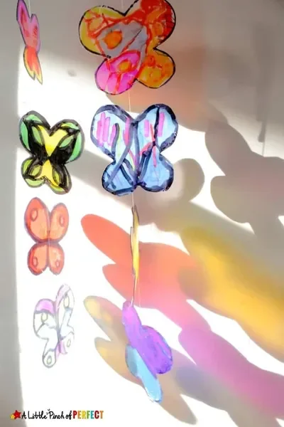Translucent butterflies made from milk jugs hang from a string in the sunshine, casting colorful shadows.