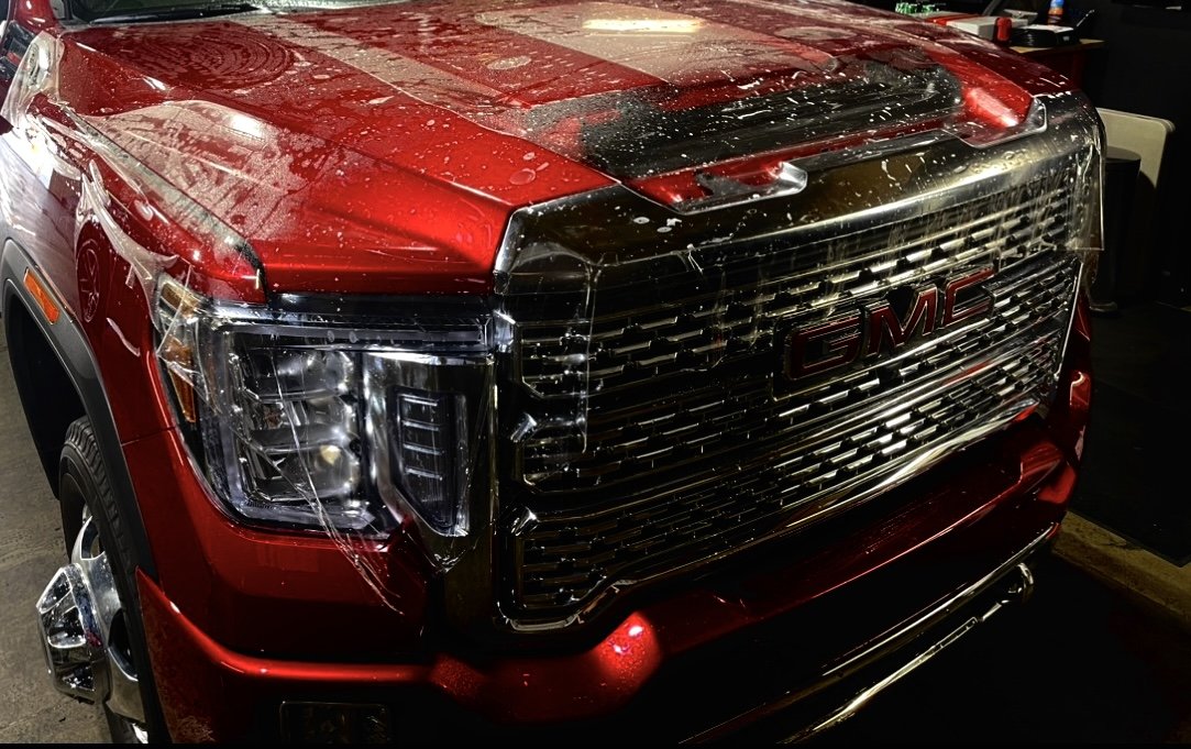 Front view of a red GMC truck with a damaged, cracked windshield and a black grille.