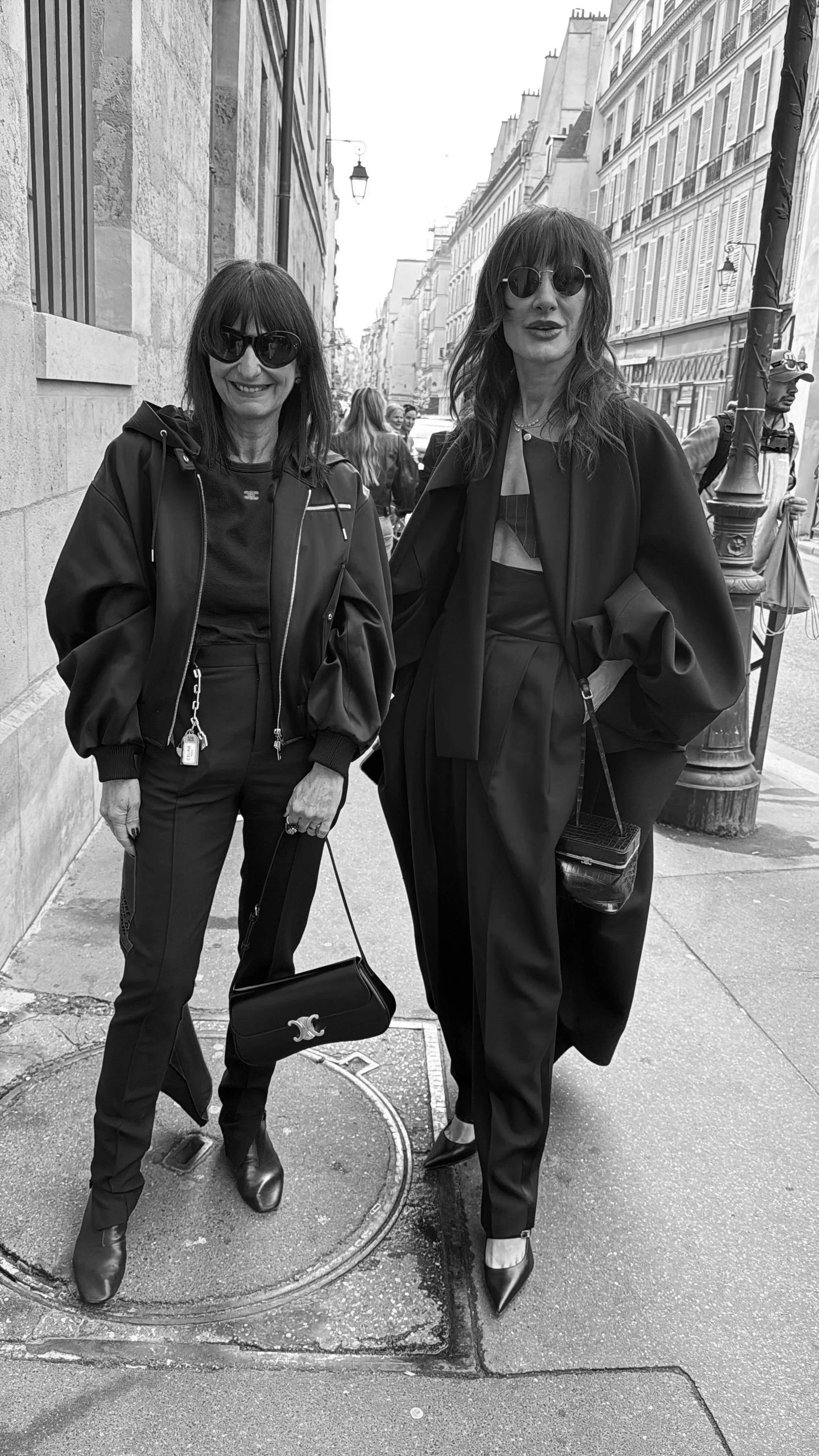 Uutiset stailauksen ja muodin parista. Kaksi naista seisoo ennen muotinäytöstä Pariisin kaduilla.