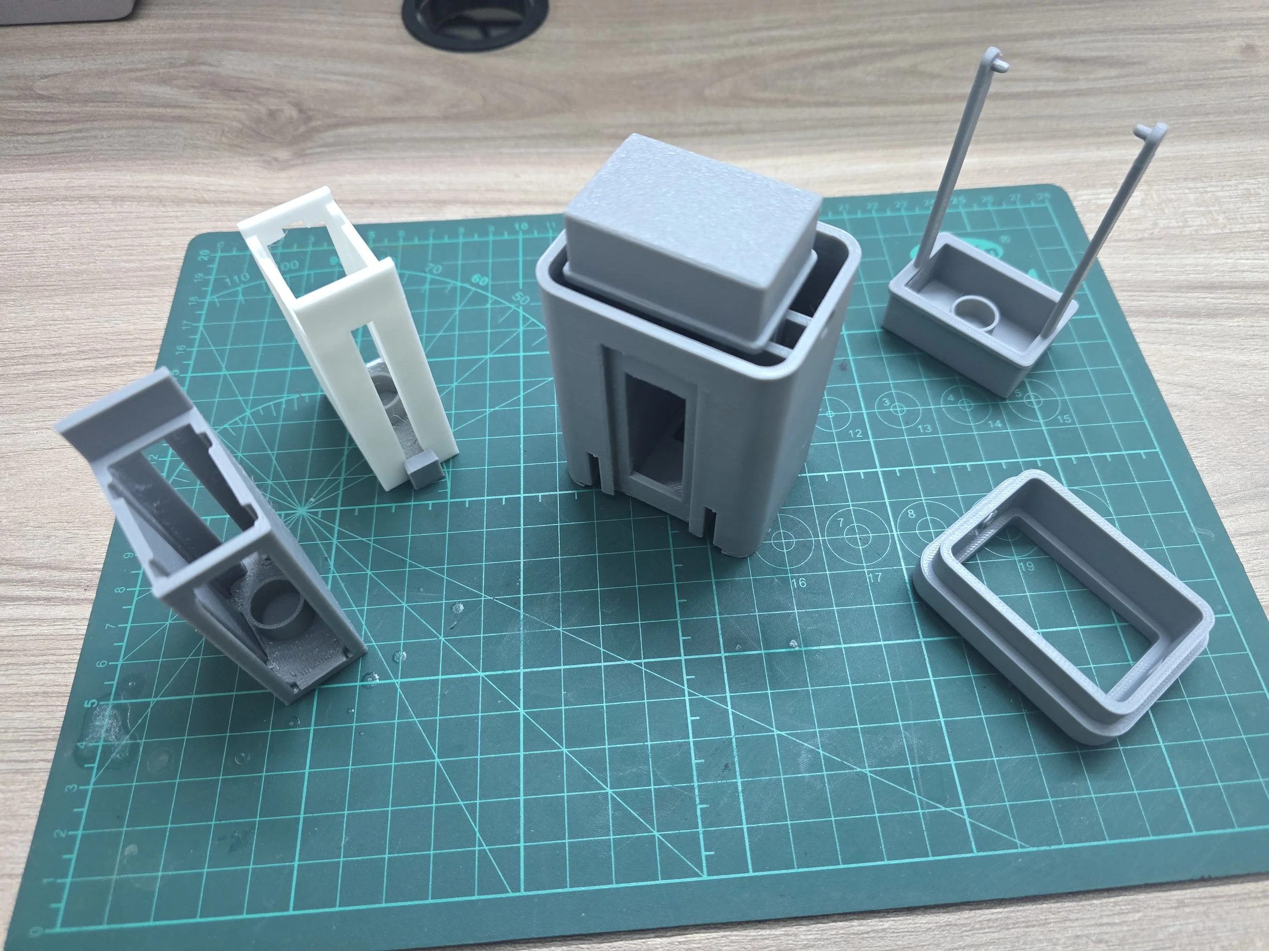 Several 3D-printed plastic components of various shapes and sizes placed on a green cutting mat on a wooden surface.