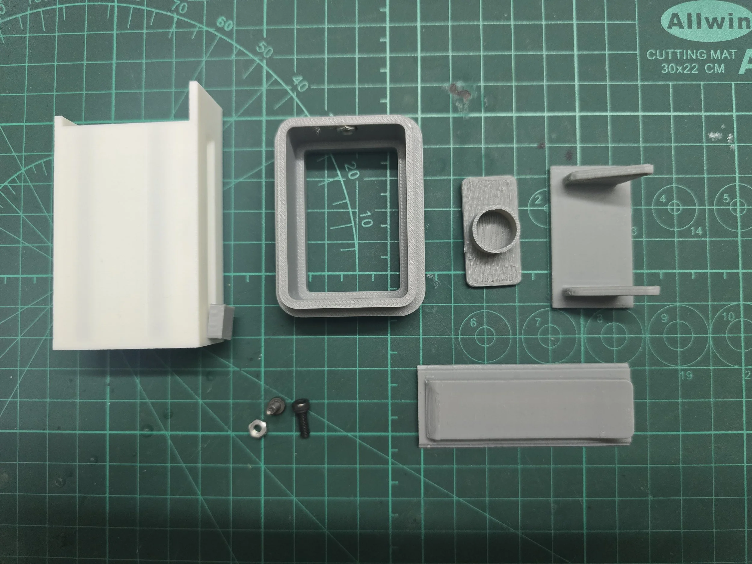Disassembled 3D printed parts, screws, and nuts on a green cutting mat.