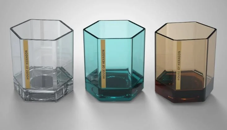 Three hexagonal glasses with different colors—clear, teal, and amber—placed on a white surface, each with a yellow vertical label reading "HOUSE OF HEXAGON."