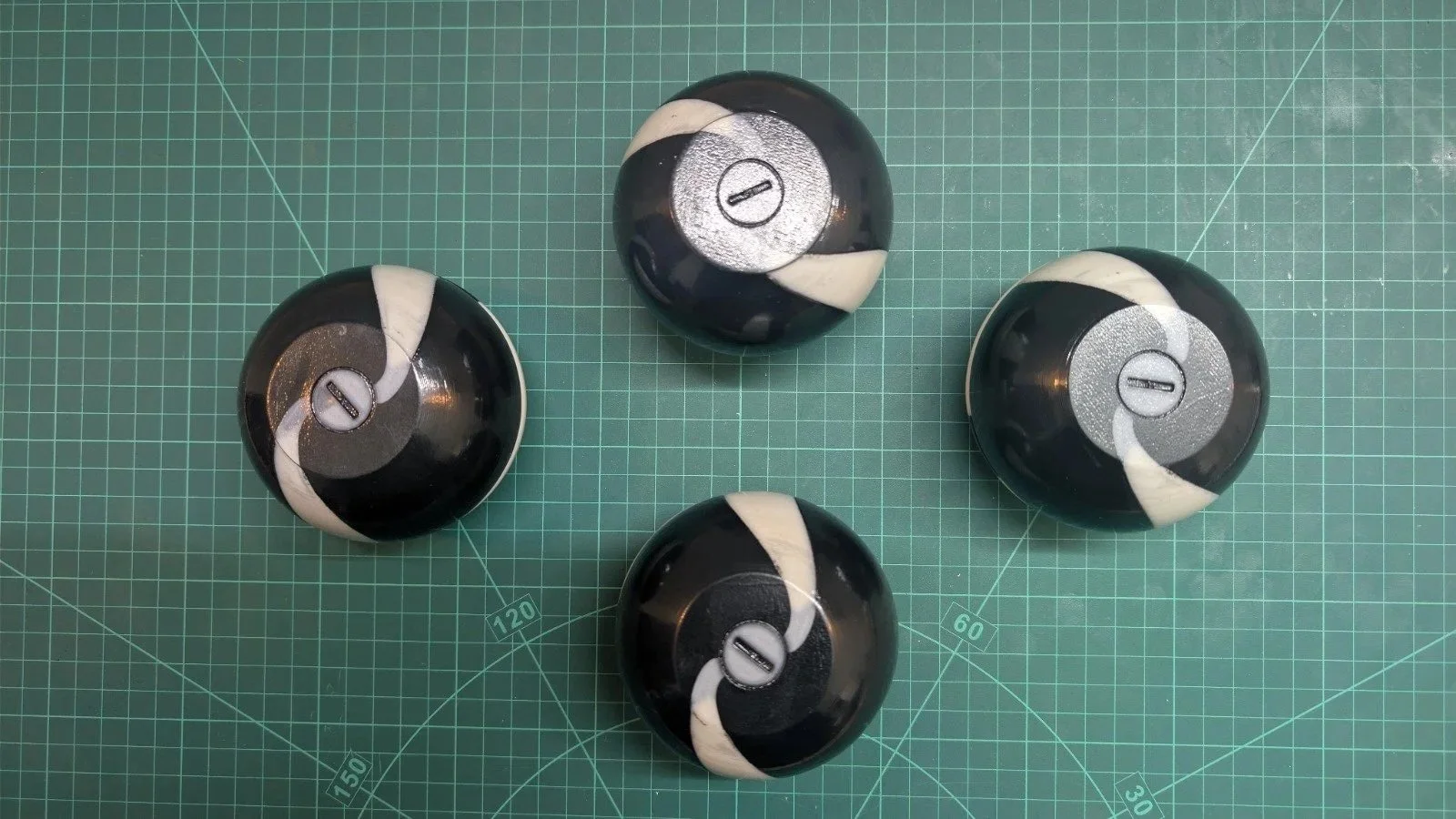 Four black and white billiard balls from a pool set on a green cutting mat.
