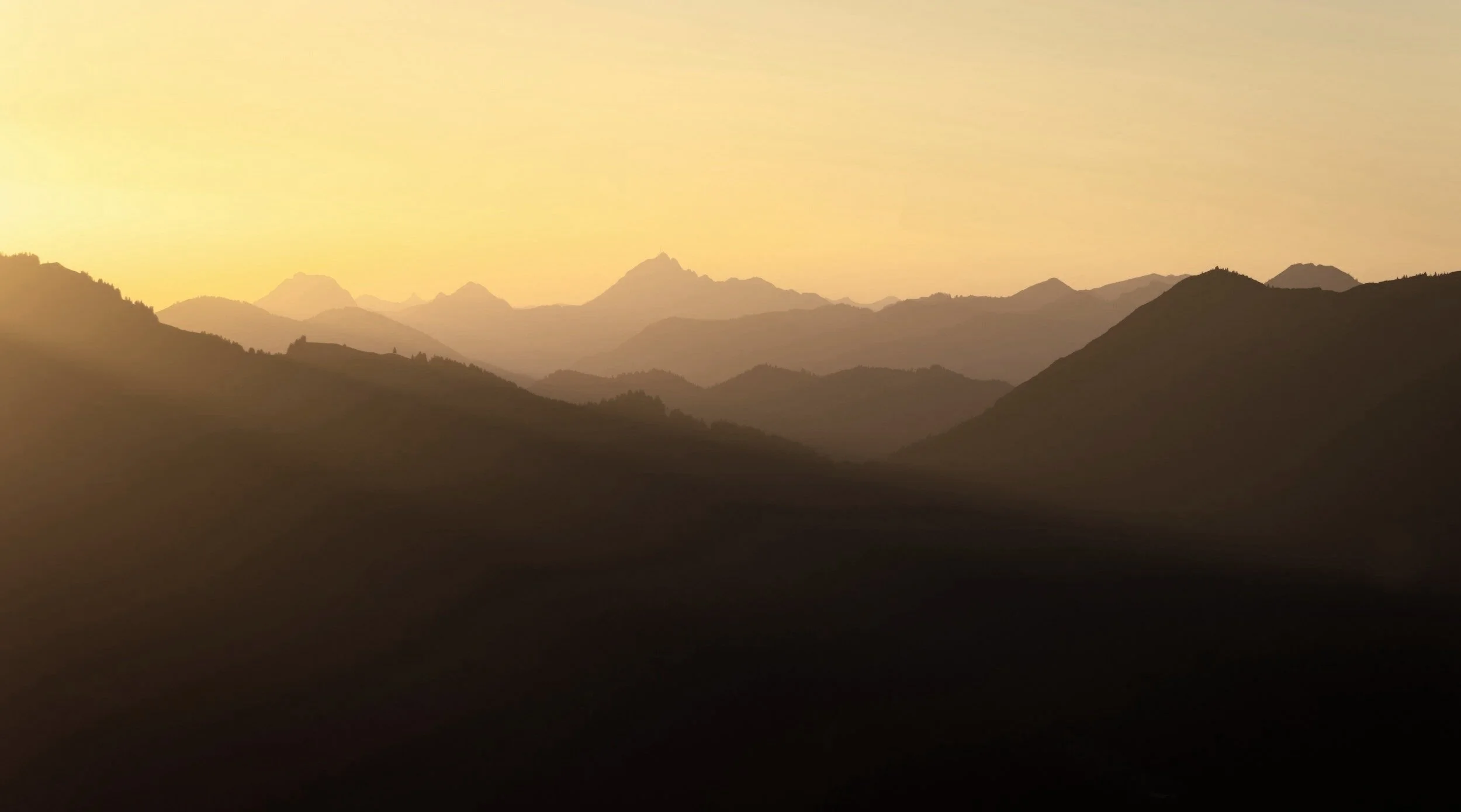 Silhouetted mountain range at sunset with a golden sky, layered mountain peaks fading into the distance.