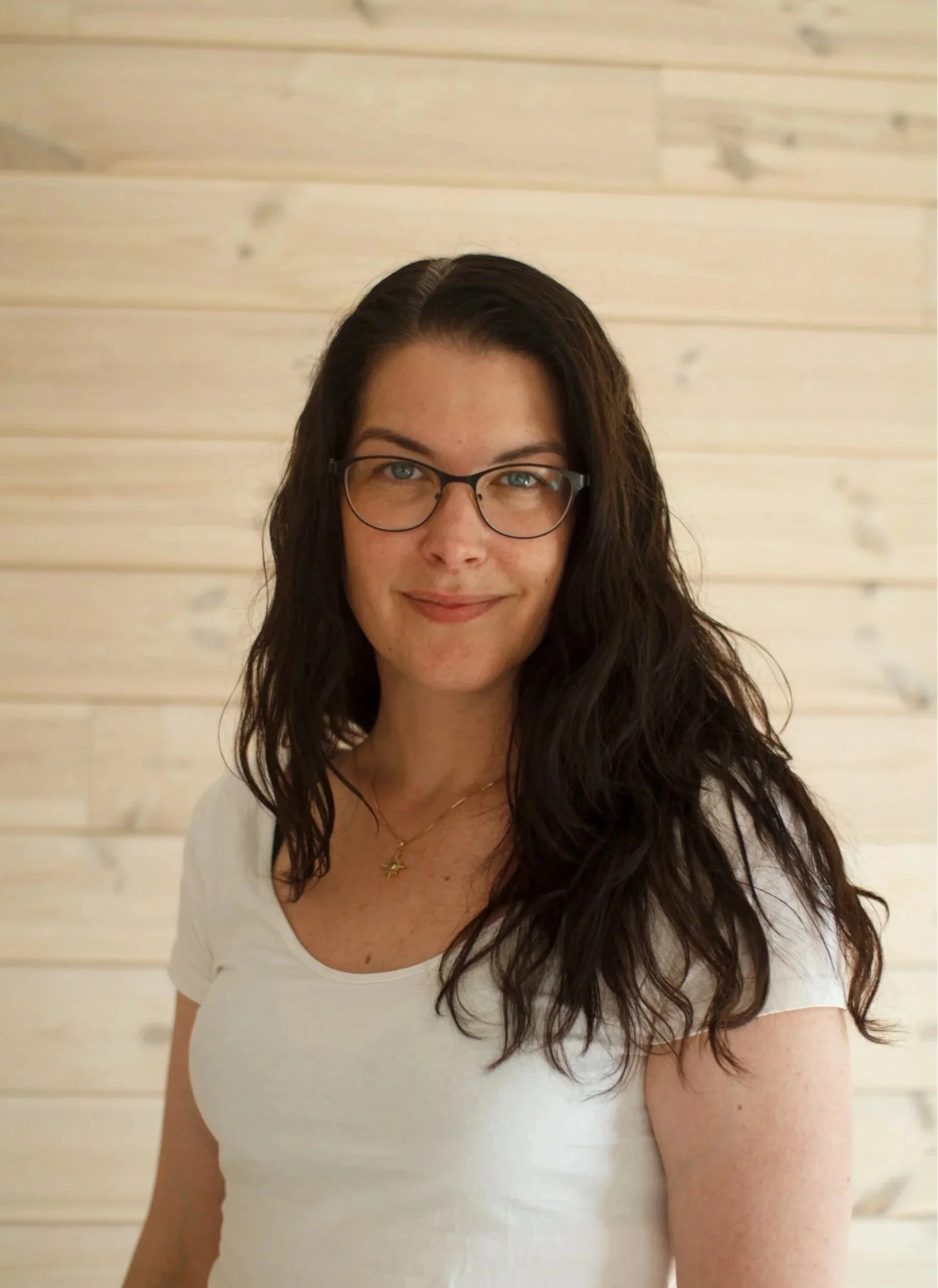 Bild av Christin Ung - Embodiment Coach. Kvinna i 30-årsåldern med mörkt långt hår och glasögon som ler och tittar in i kameran