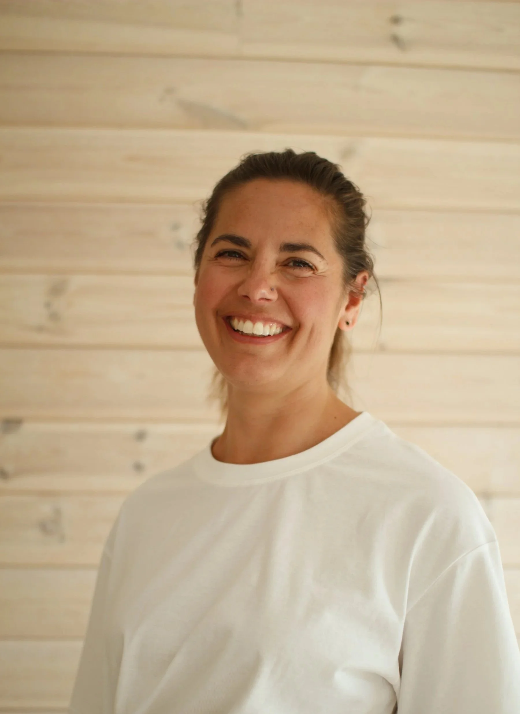 Bild av Hanna Schönborg - Embodiment Coach. Kvinna i 30-årsåldern med brunt uppsatt hår som skrattar och tittar in i kameran