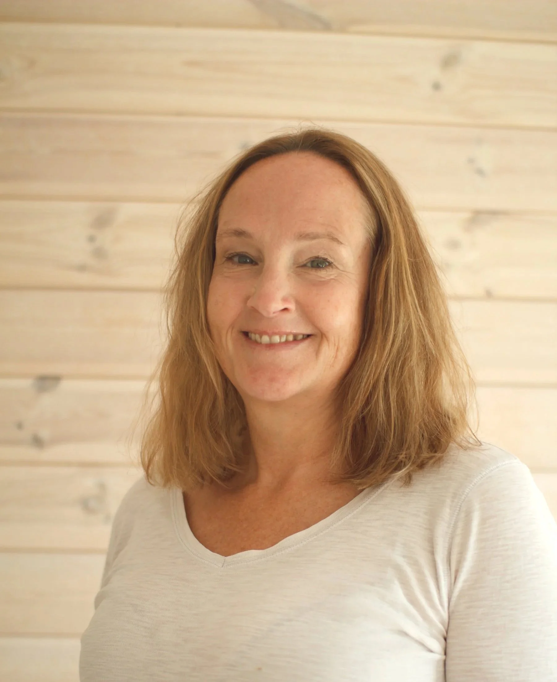 Bild av Sara Hellberg - Embodiment coach. Kvinna i 45-50 årsåldern med blont axellångt hår som ler och tittar in i kameran