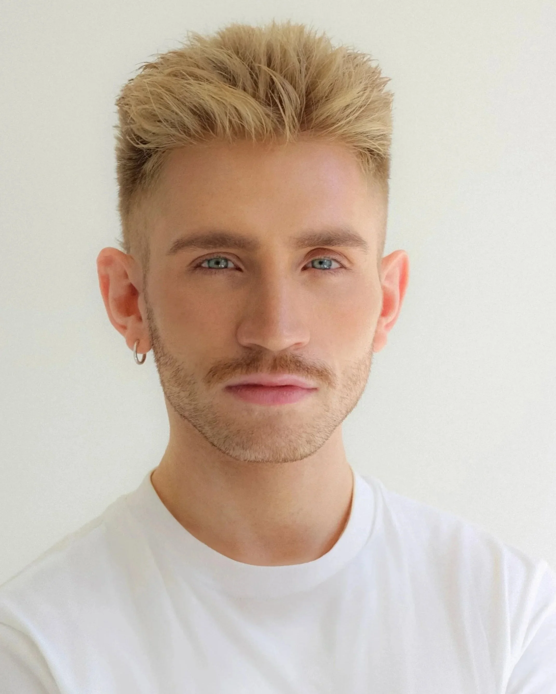 Close-up of a young man with blonde hair, blue eyes, and a white shirt against a white background.