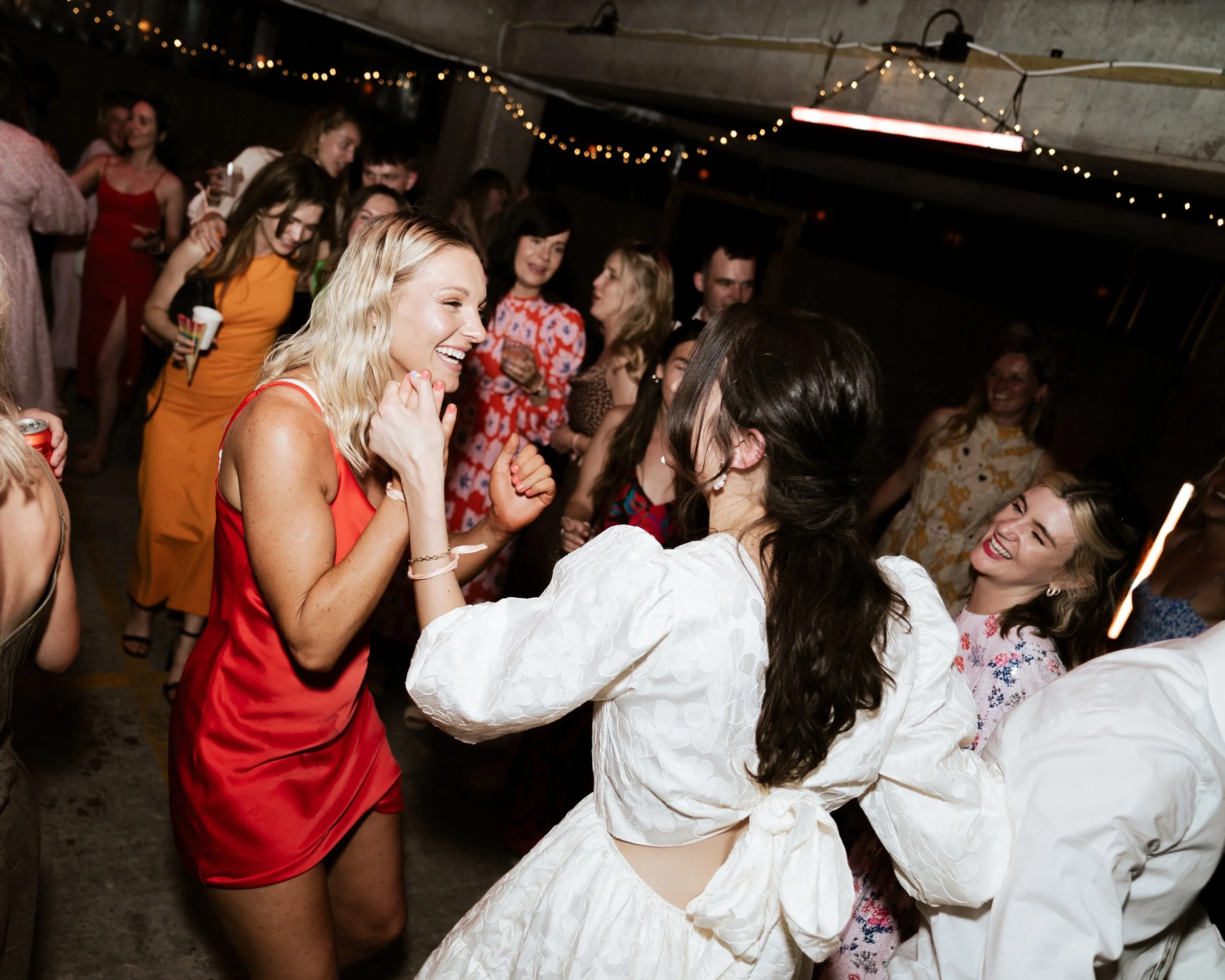 Group of women dancing and enjoying at a party with string lights in the background.