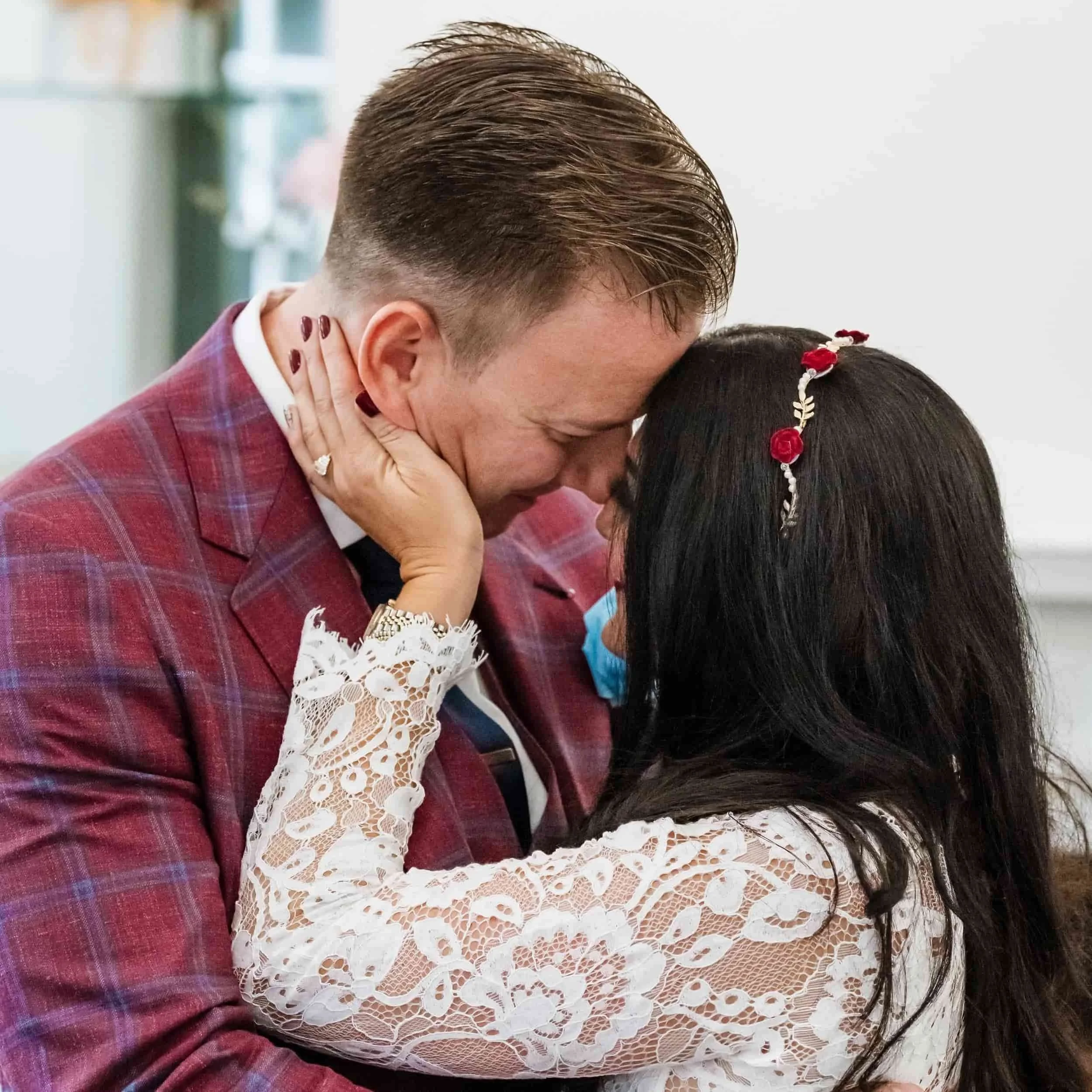 A bride and groom are having an intimate moment. The birde is holding the gooms face and their foreheads are touching.