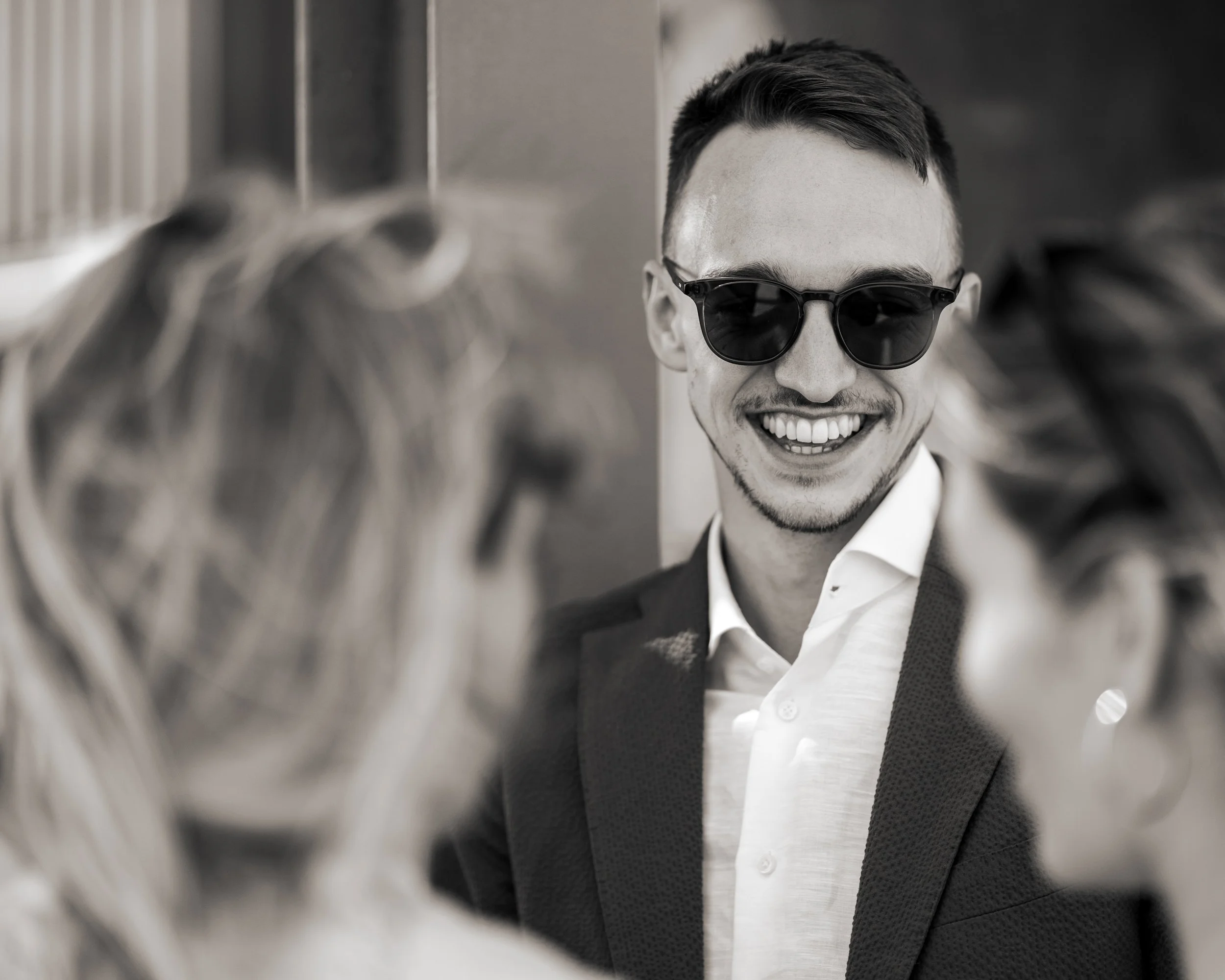A man wearing sunglasses and a suit smiling at a woman with curly hair.