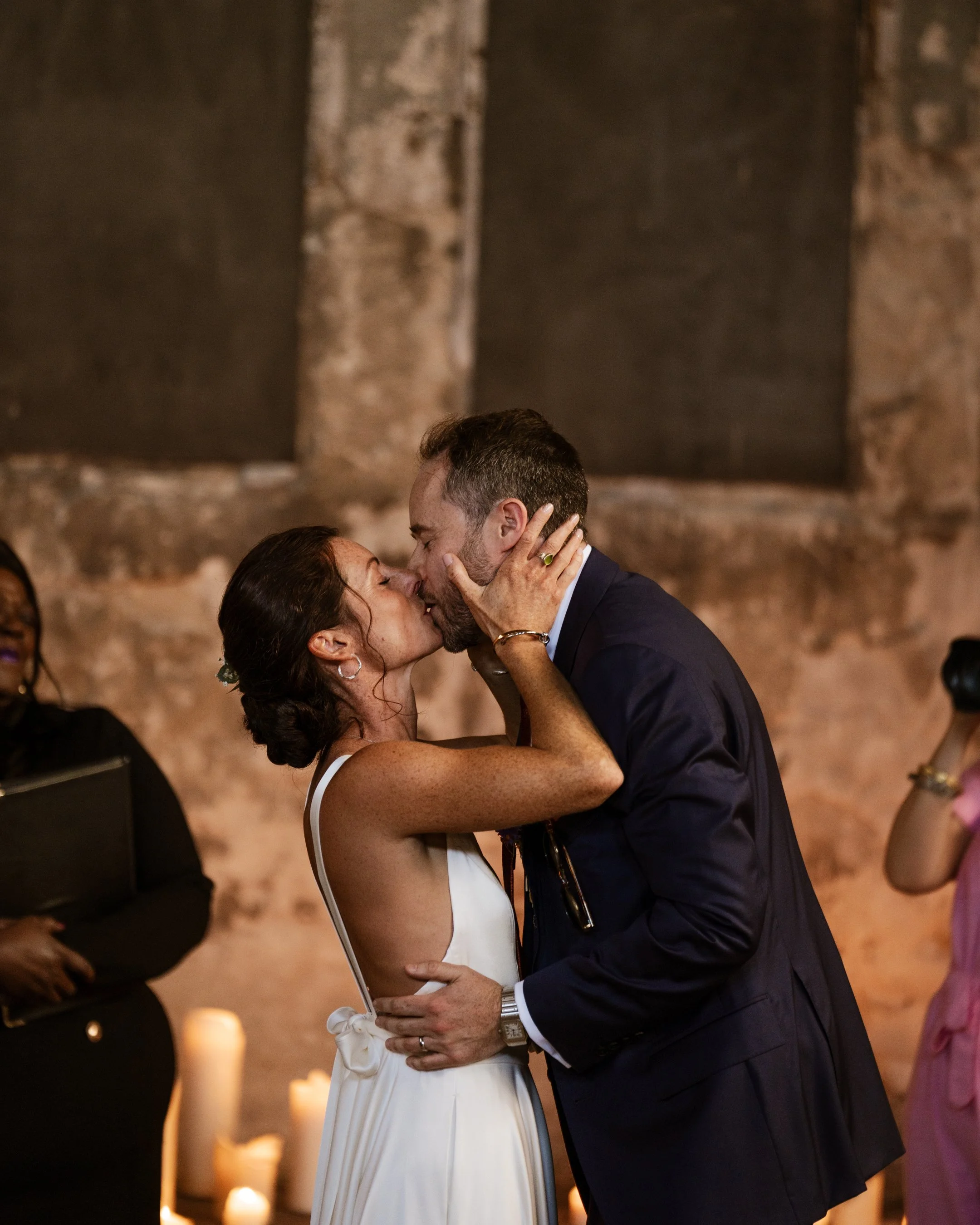 A newlywed couple sharing a kiss during their wedding reception, with candles in the background.