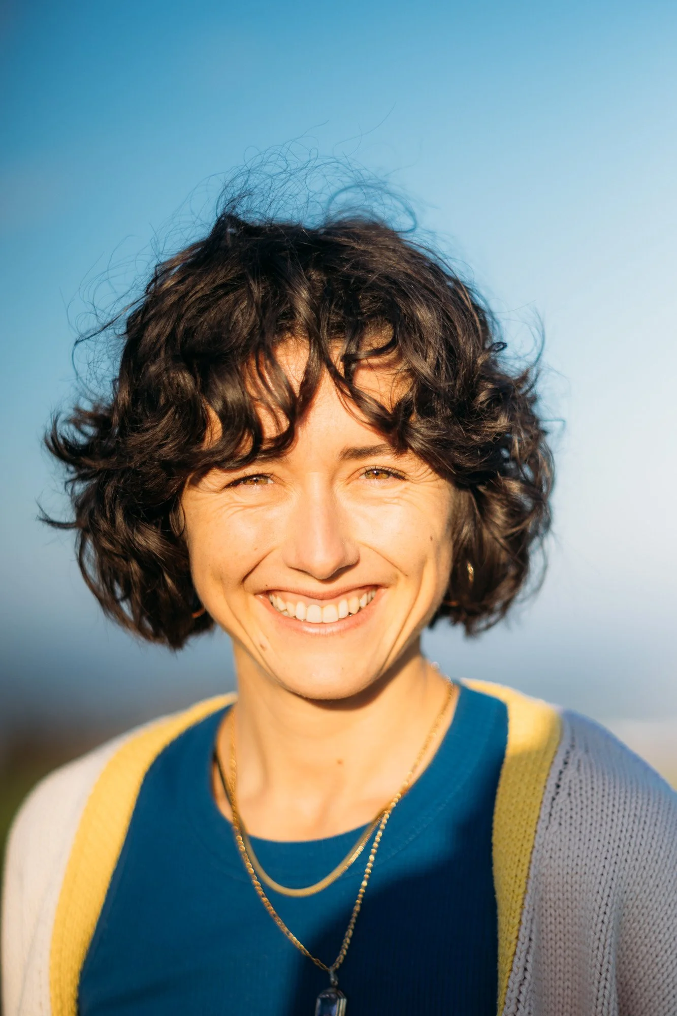 Sarah Baumer, Heilpraktikerin für Psychotherapie, die in die Kamera schaut; trägt eine blaue Bluse und eine Kette, vor einem klaren blauen Himmel.