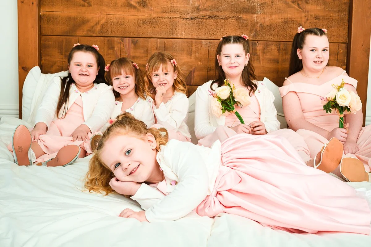 Group of girls in pink dresses with flower bouquets lying on a bed.