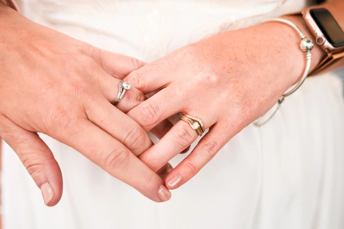 close-up of hands wearing wedding rings and bracelets, white dress background