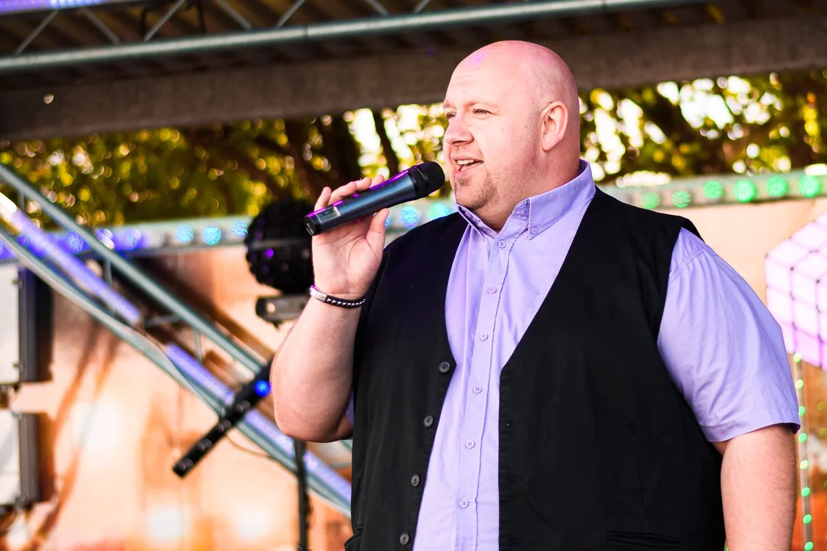 Person singing into a microphone on stage with bright lights.