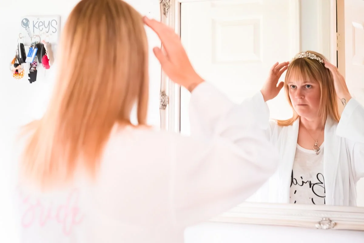 Woman in white robe adjusting tiara in mirror reflection, key holder on wall.
