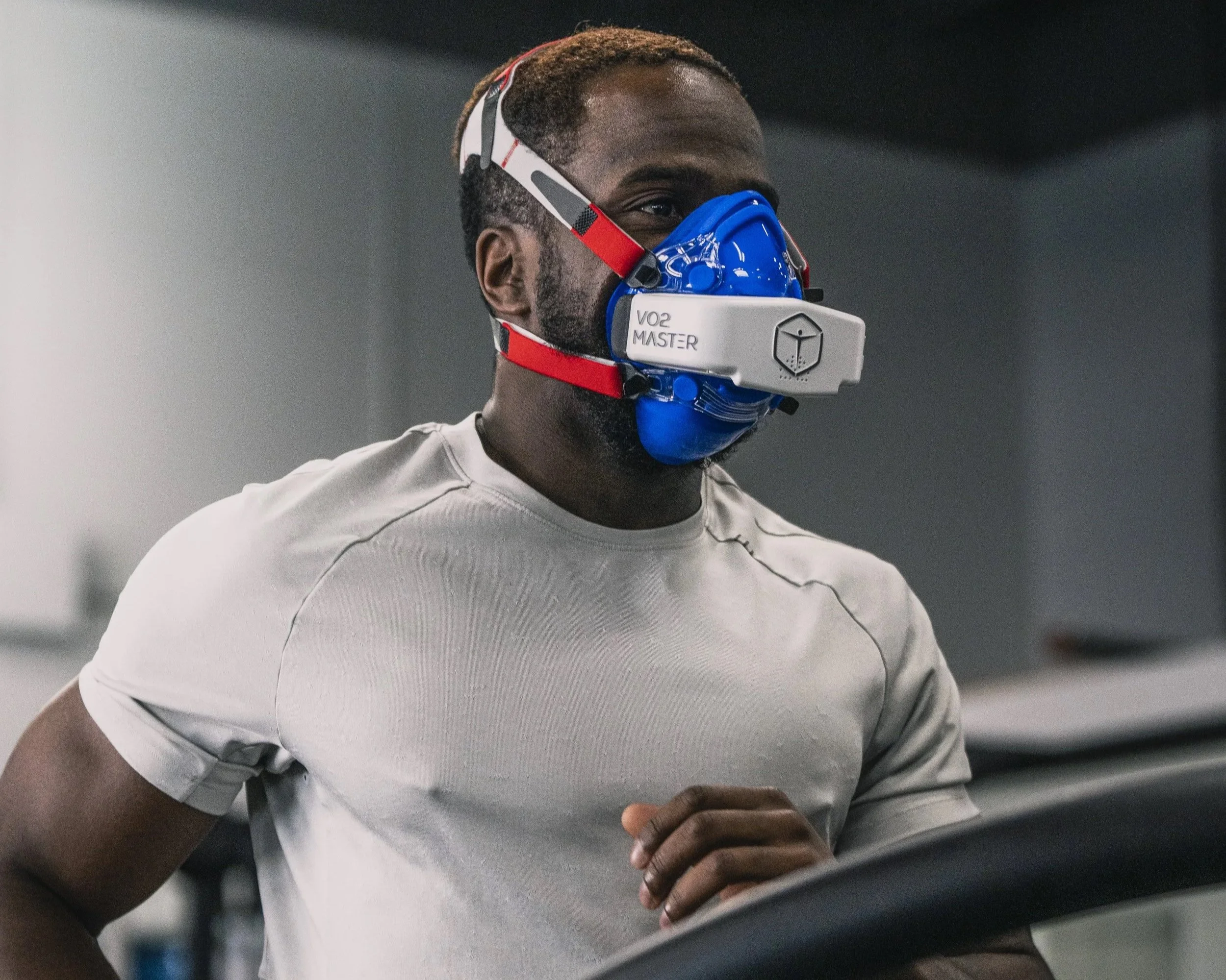 A man running on a treadmill in a gym, wearing a mask labeled VO2 MASTER.
