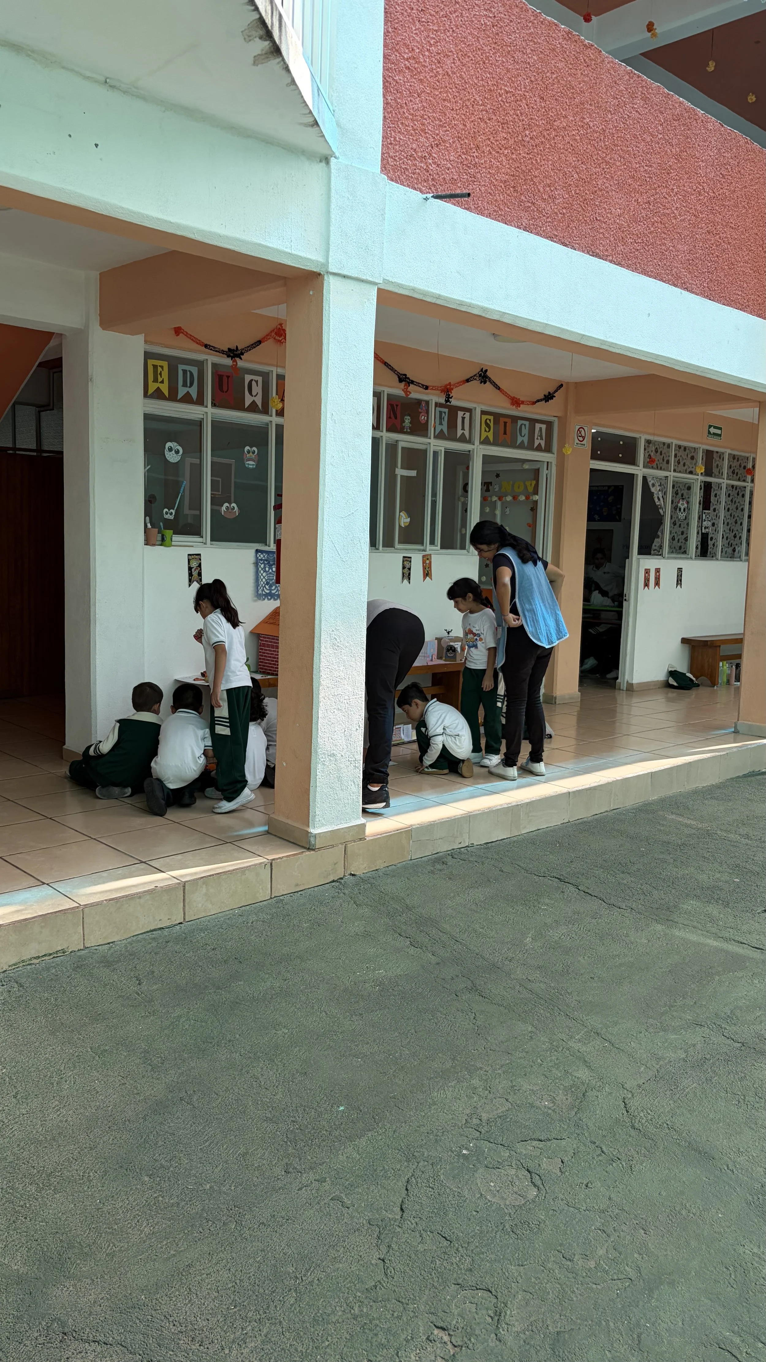 Niños y maestras en un aula decorada con temática de Día de Muertos, participando en una actividad educativa.