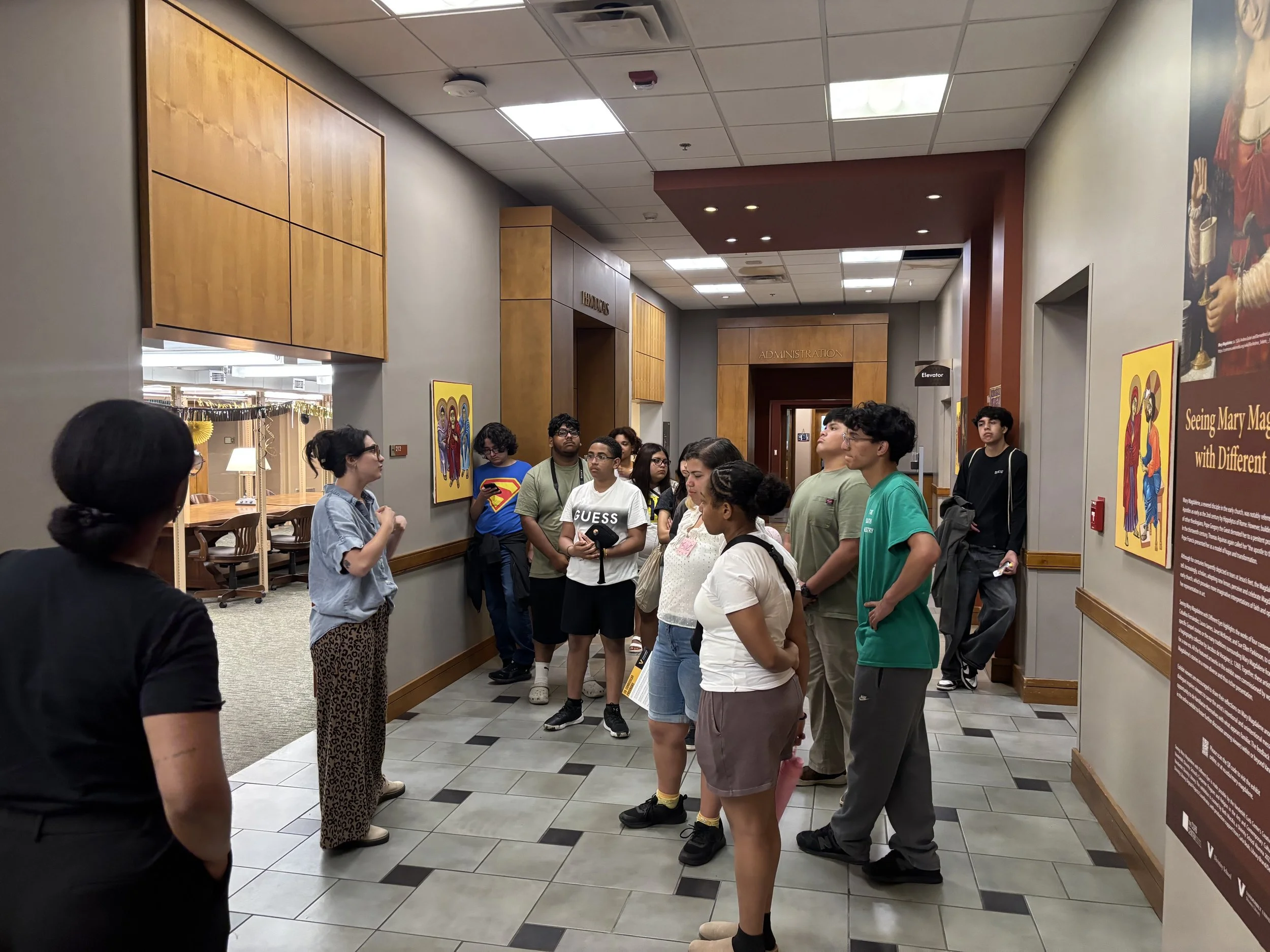 HYLA youth listen to a guided tour of Vanderbilt Divinity School, surrounded by religious artwork, informational displays, and wooden wall panels.