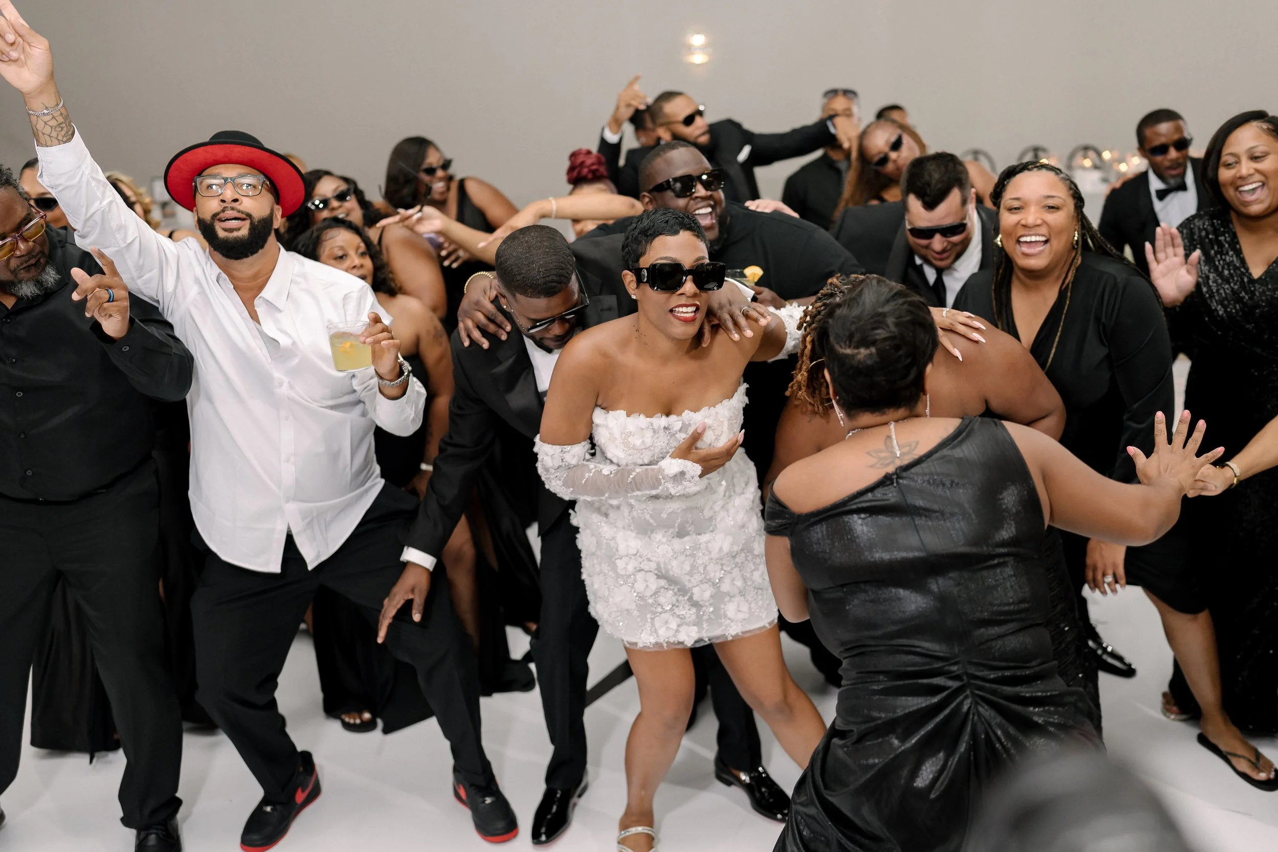People dancing and enjoying themselves at a wedding reception with some wearing sunglasses.