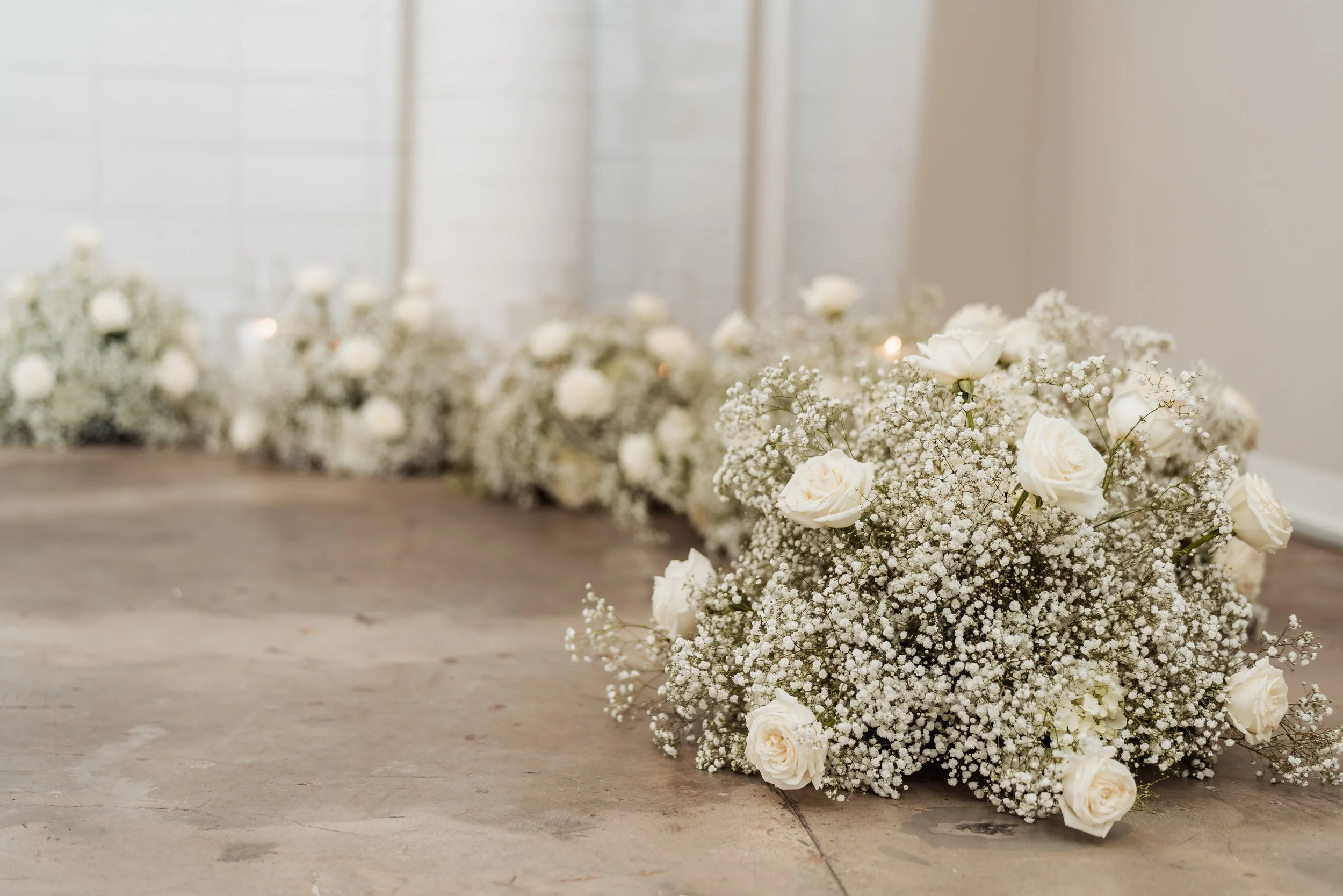 White flower arrangement with roses and baby's breath on a wooden surface, blurred background.