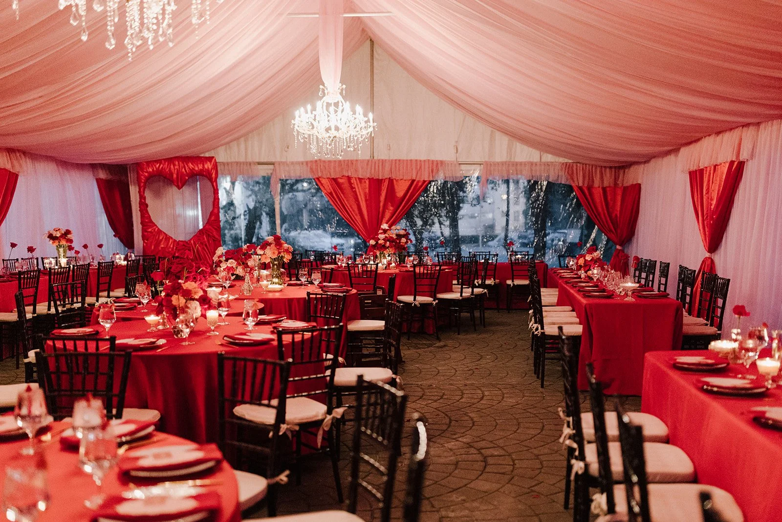 Elegant event tent with pink drapery, chandeliers, and round tables decorated with pink flowers and candles.