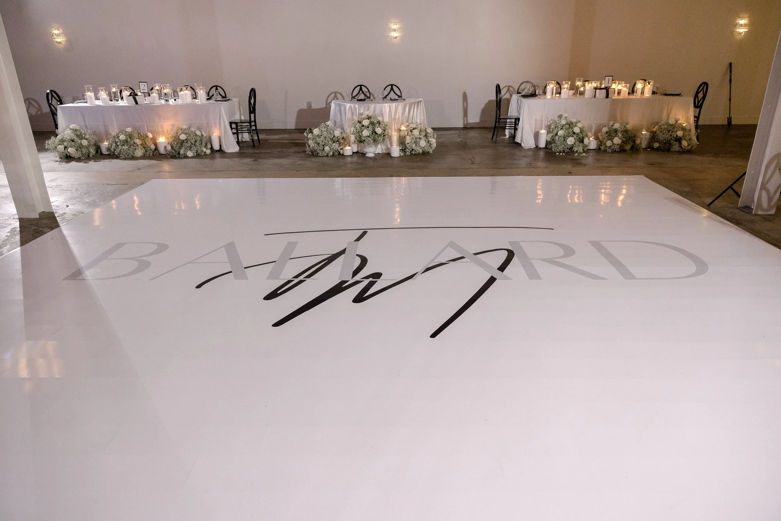 Wedding reception area with decorated tables, floral arrangements, and candles on the floor.