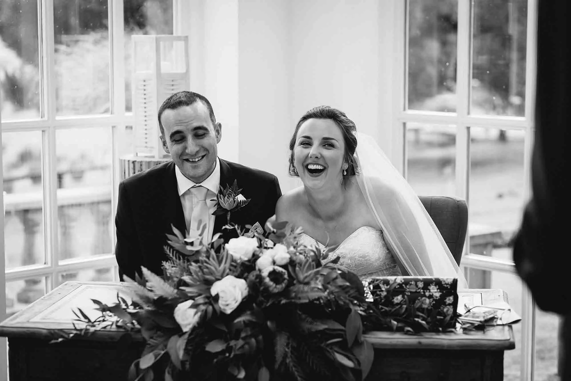 The bride and groom sharing a joke at the signing of the register during their wedding at Woodhill Hall.