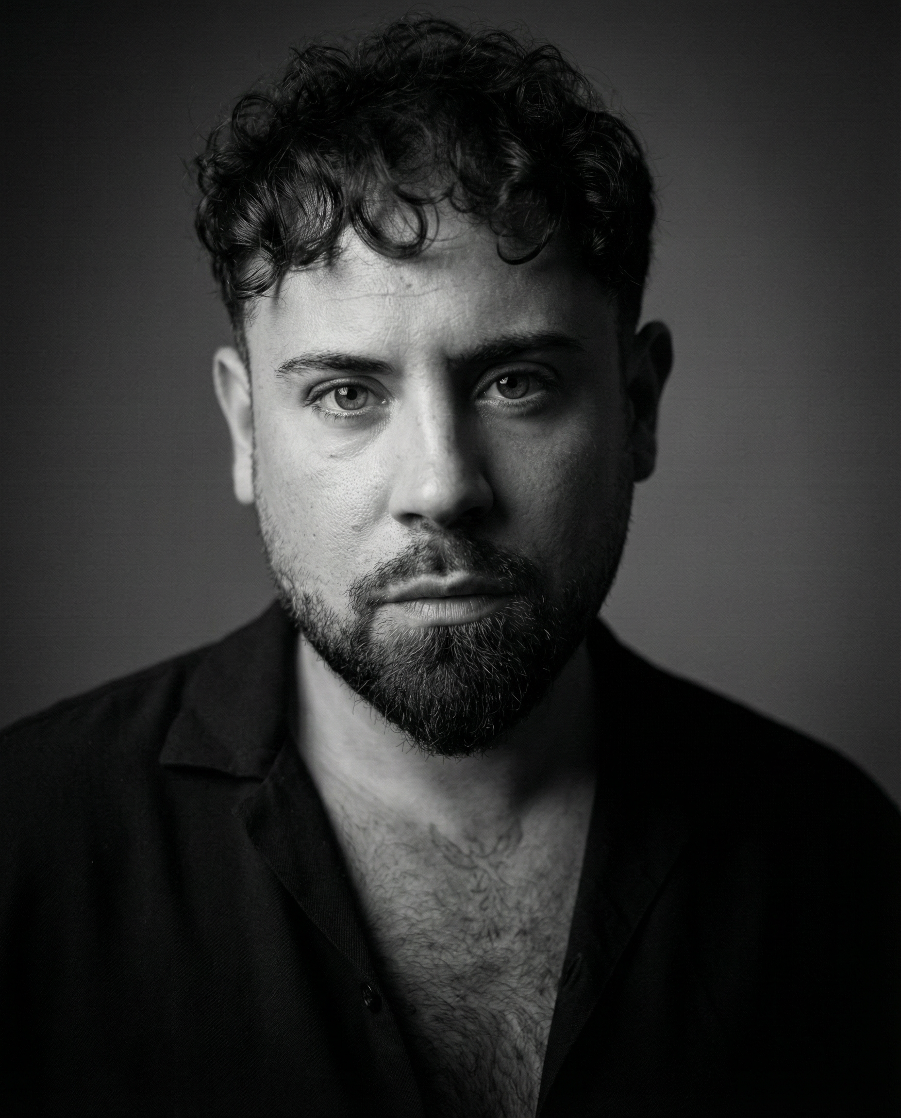 Ritratto in bianco e nero di un uomo con capelli ricci e barba, che indossa una camicia aperta.