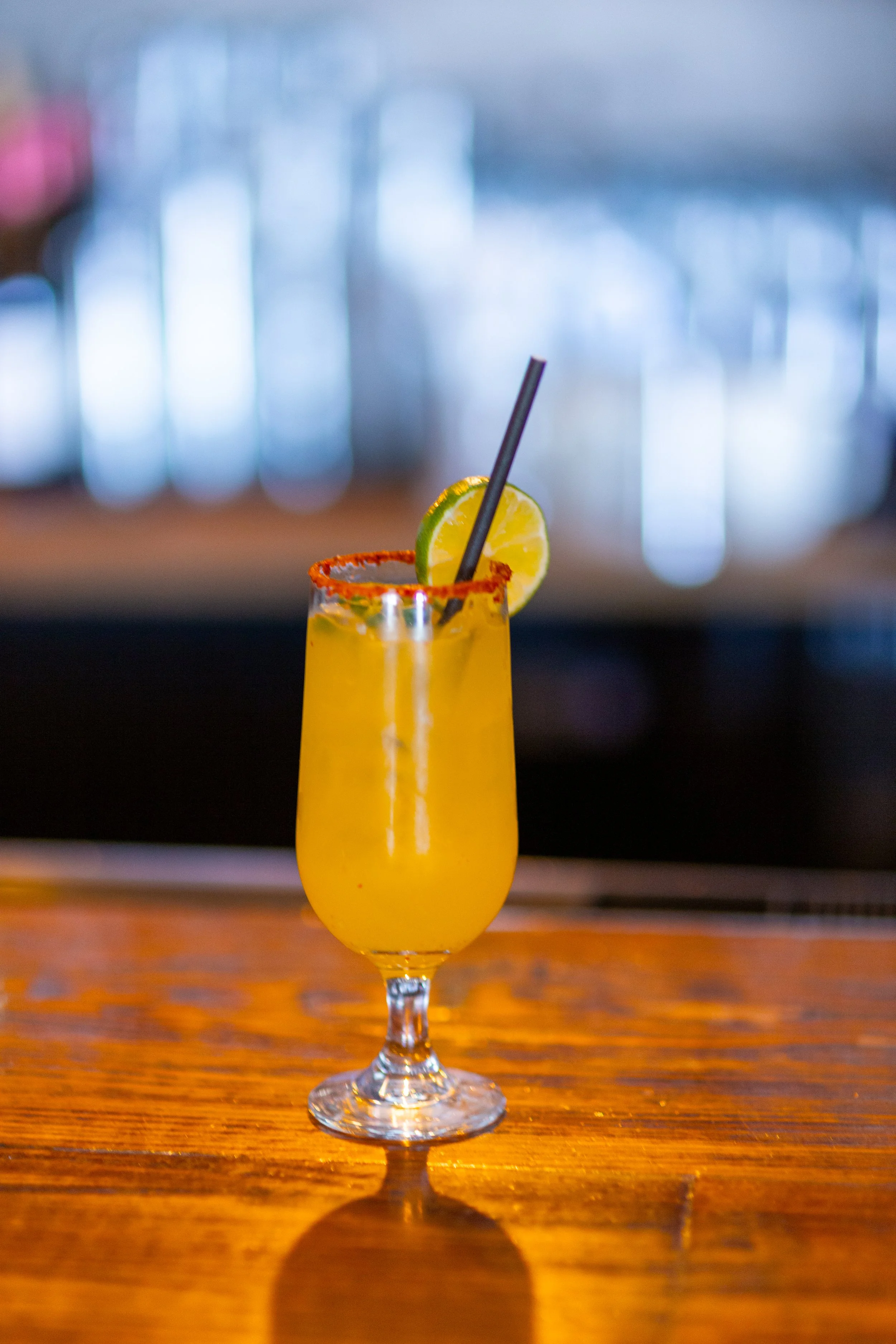 Yellow cocktail with lime garnish in a glass on a bar table