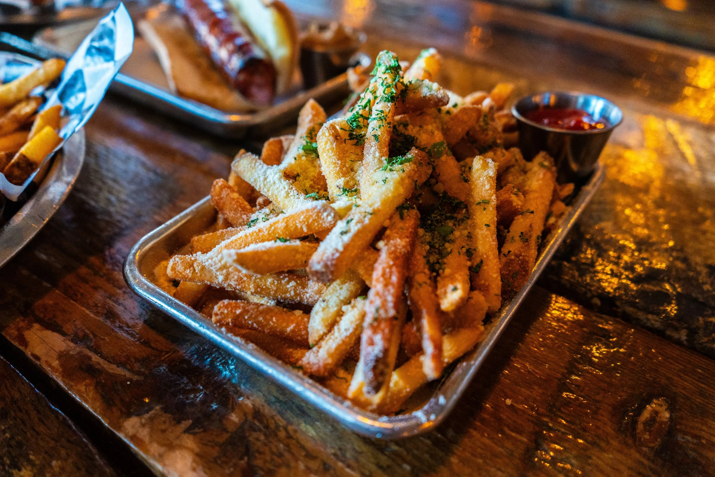 A plate of seasoned fries topped with herbs and grated cheese, served with a side of ketchup on a wooden table.