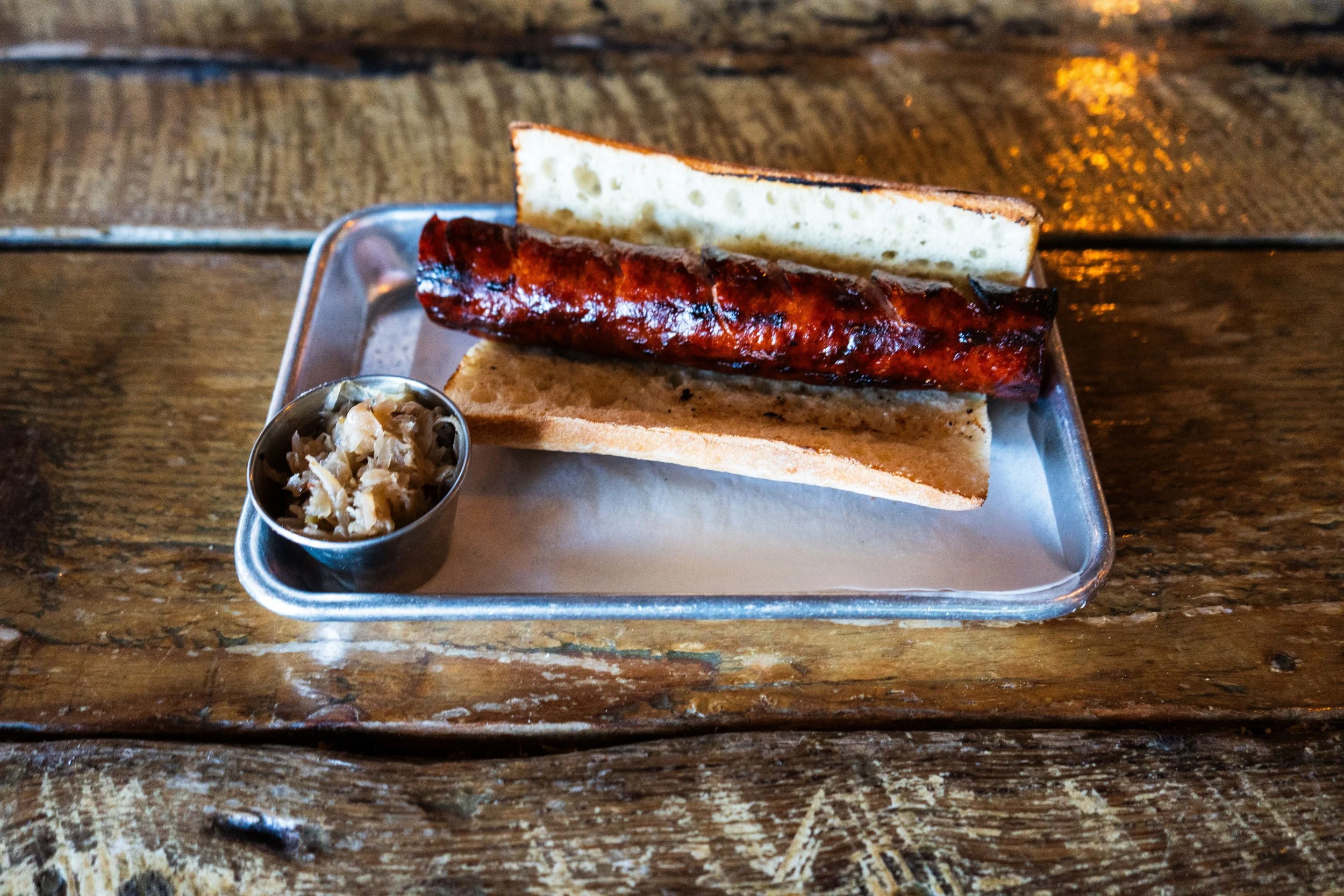 Sausage in a sliced baguette on a metal tray with a side of sauerkraut.