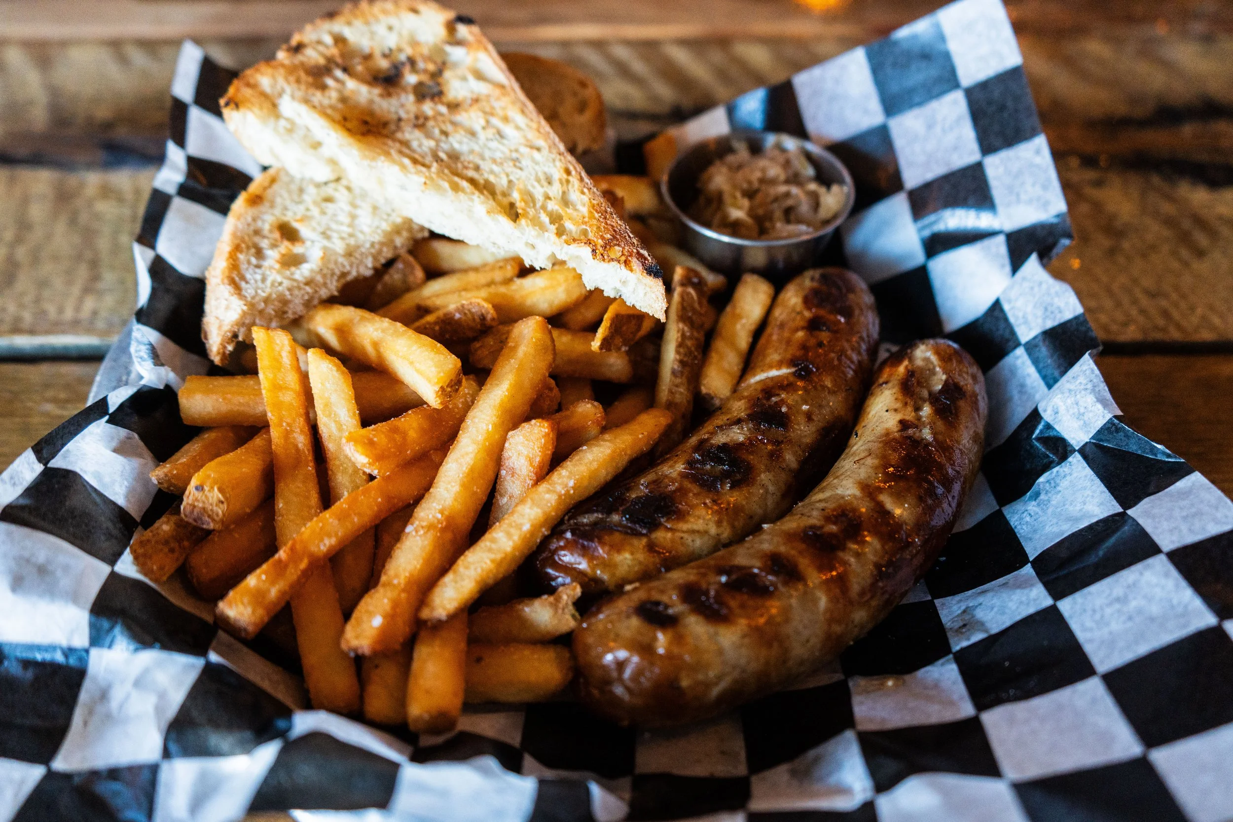 Grilled sausages with fries, toast, and sauerkraut on checkered paper.