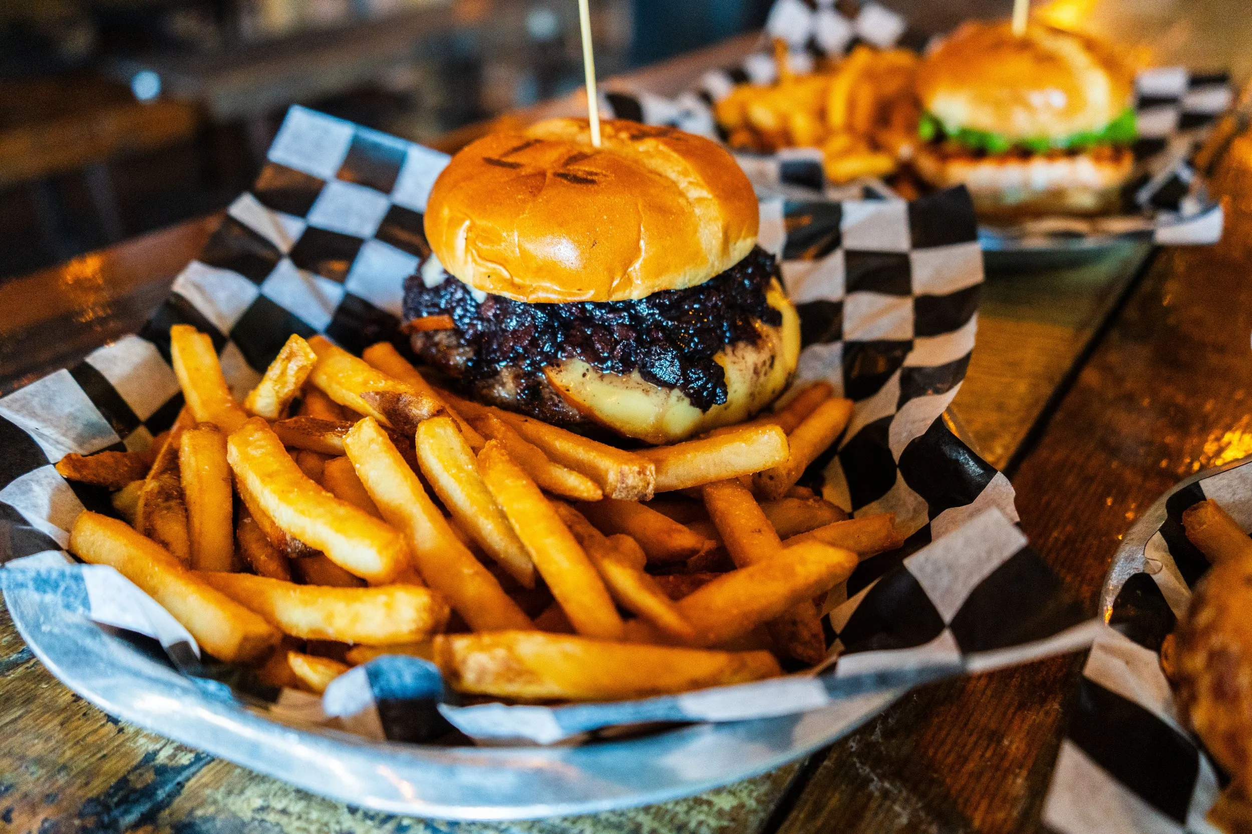 A hamburger with melted cheese and caramelized onions on a bun, served with a side of French fries on a black and white checkered paper.