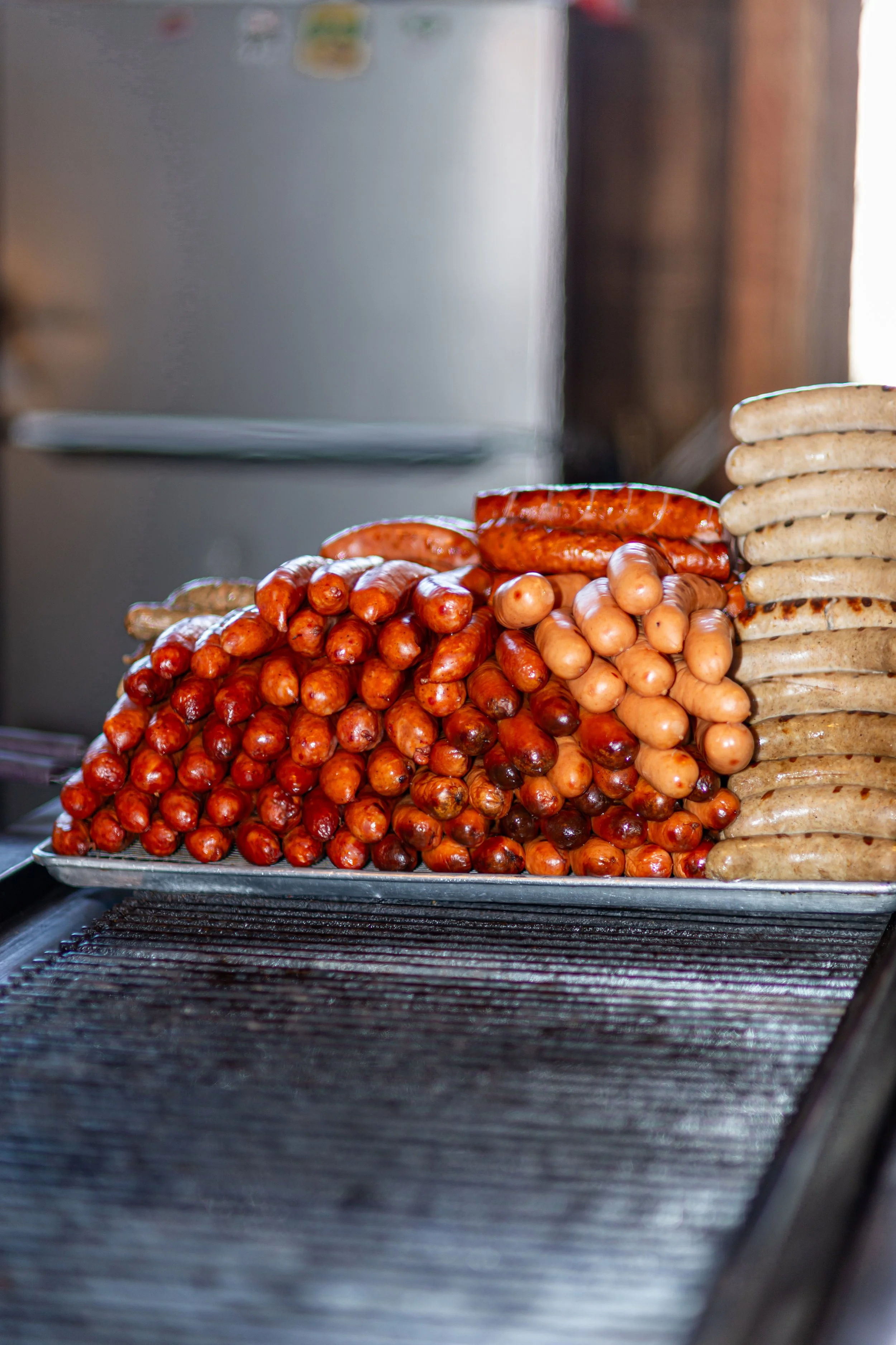 Various types of grilled sausages displayed on a tray in a kitchen setting.