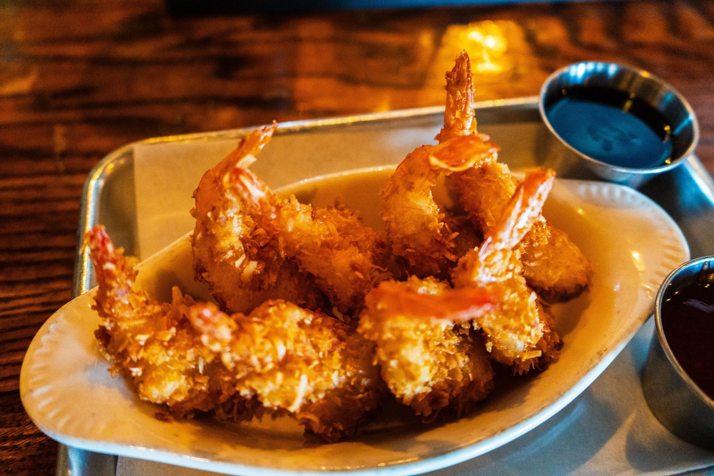 Coconut shrimp served on a white dish with two small sauce cups on the side.