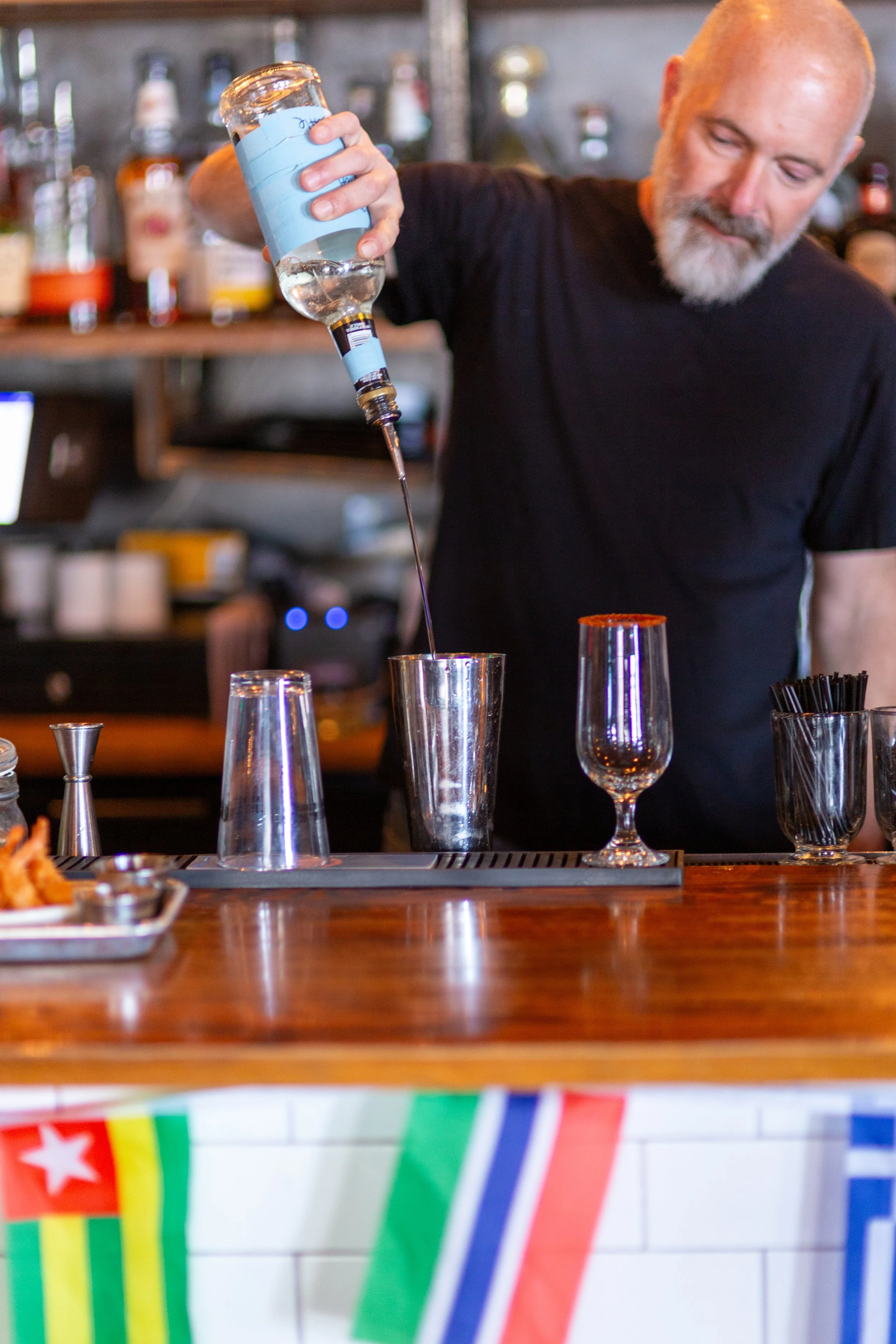 Bartender pouring liquor into a cocktail shaker at a bar.