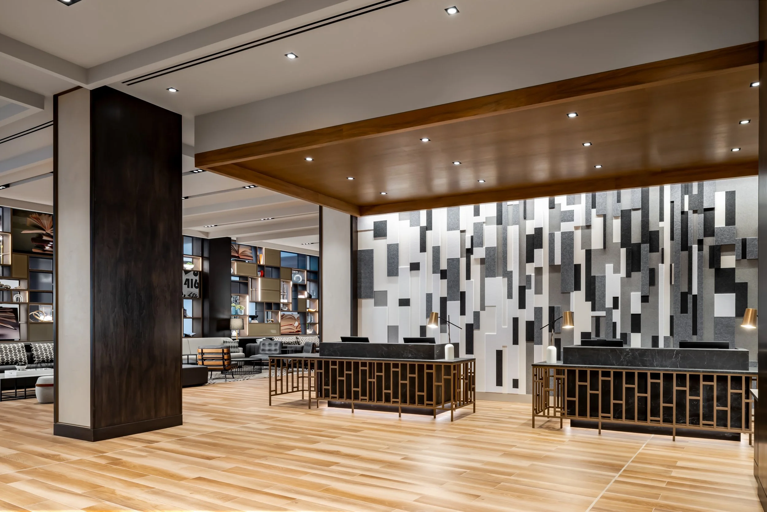 Brass and stone hotel front desks underneath wood ceiling with accent felt wall