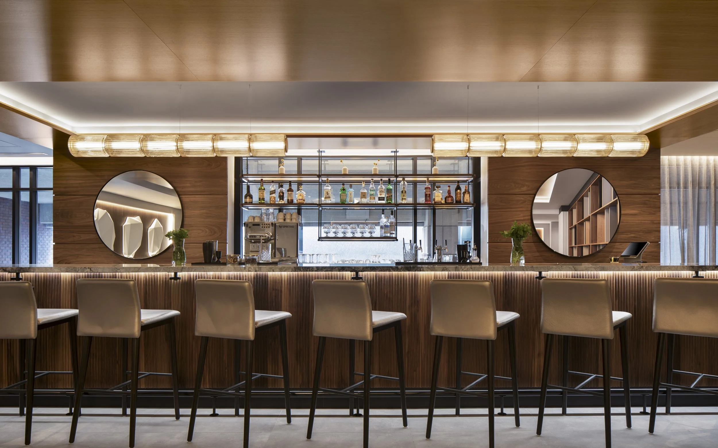 Wood stained bar with back liquor display, leather stools and linear pendant lights