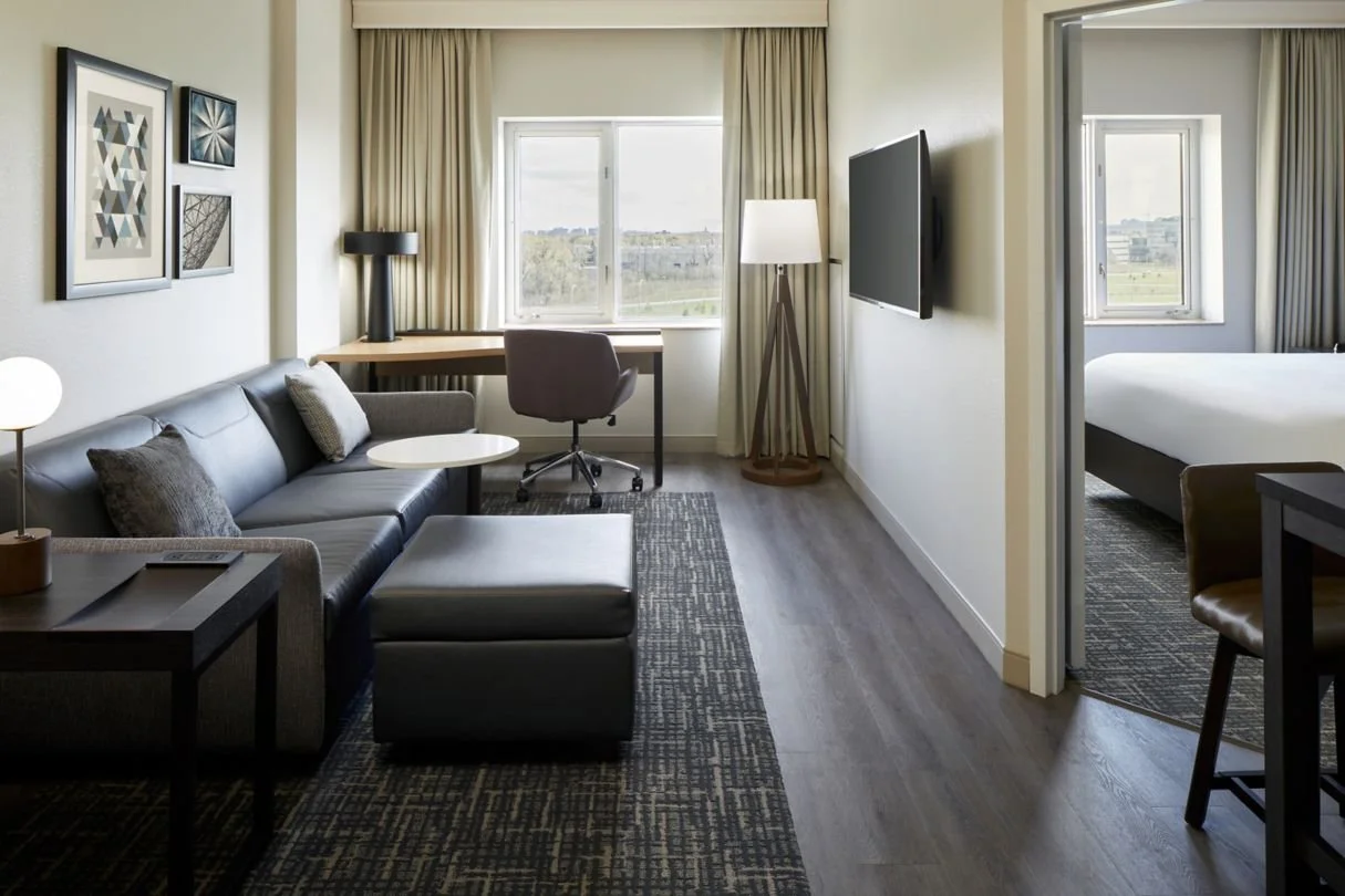 Hotel guestroom sofa area with tv and desk, all with neutral finishes
