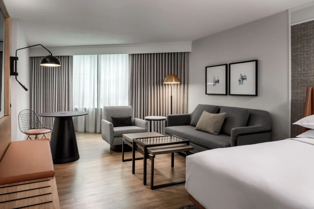 Hotel guestroom living area with upholstered seating, luggage bench, tv and desk area