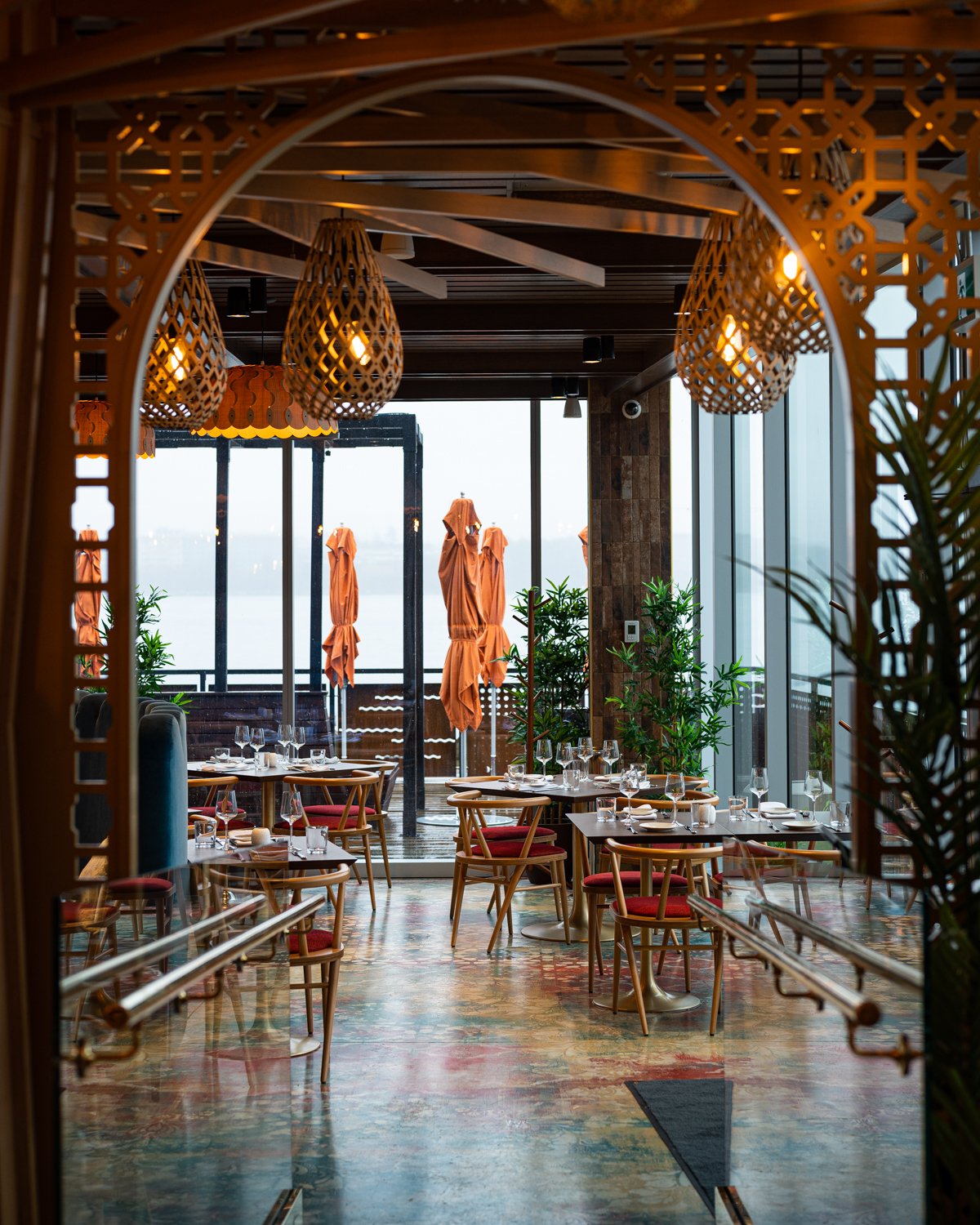 Restaurant interior with red cushioned chairs, patterned floor and large windows facing Halifax Harbour